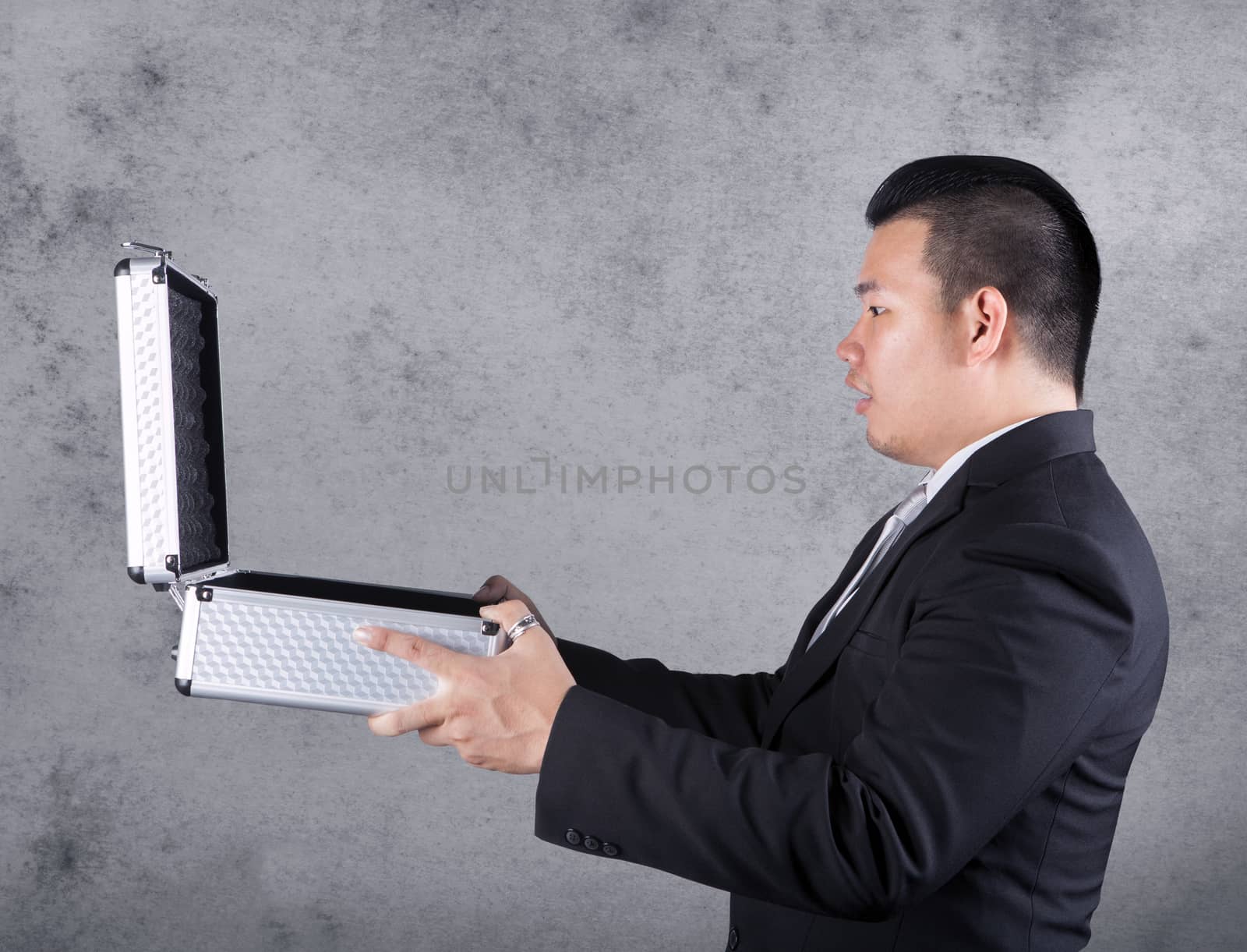 business man open metal suitcase and surprising face against empty cement wall ,with copy space to fill product 