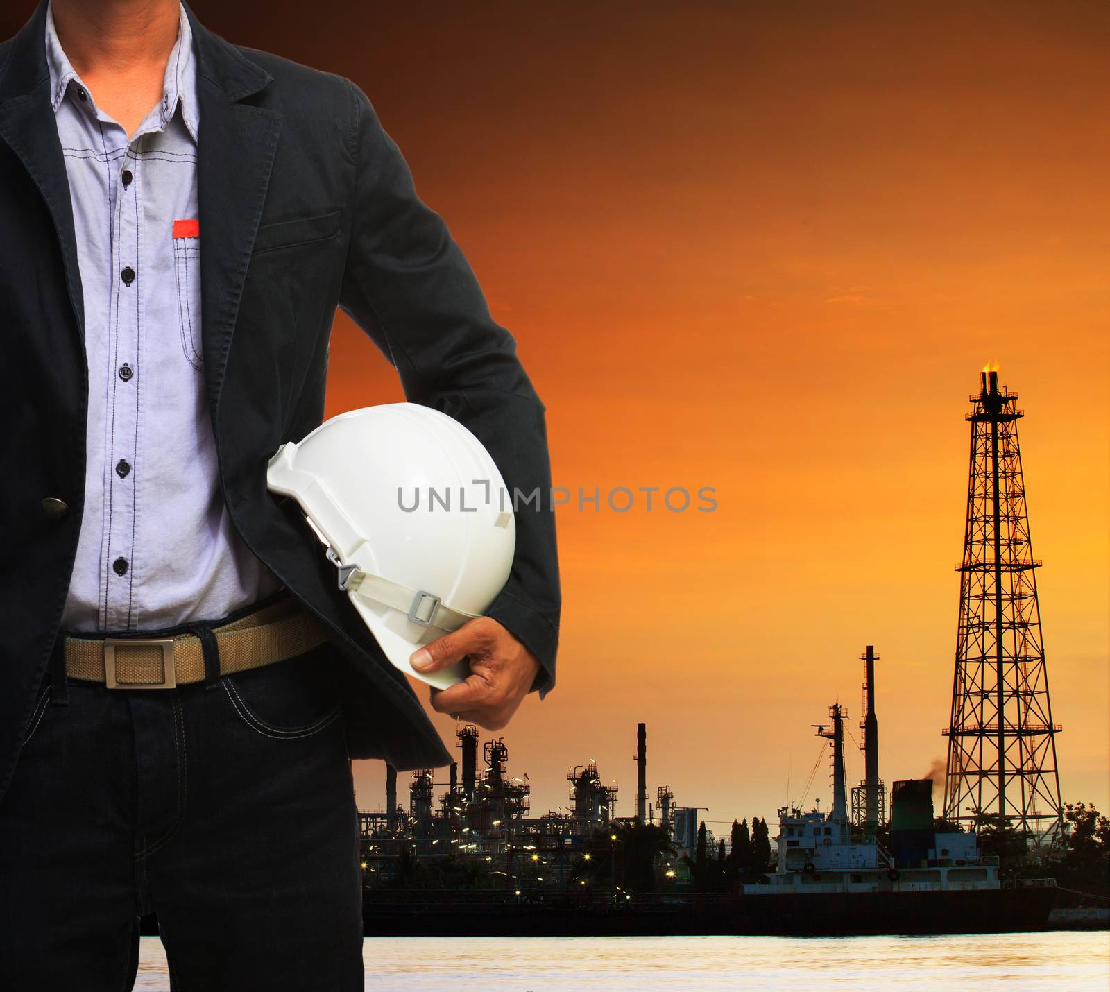 engineering man and safety helmet standing against beautiful dusky sky of oil refinery plant scene use for energy of fossil fuel and industry topic background