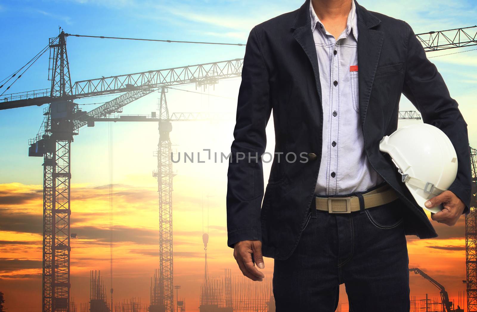 engineer man working with white safety helmet against crane and  building construction site use for civil engineering and construction industrial business