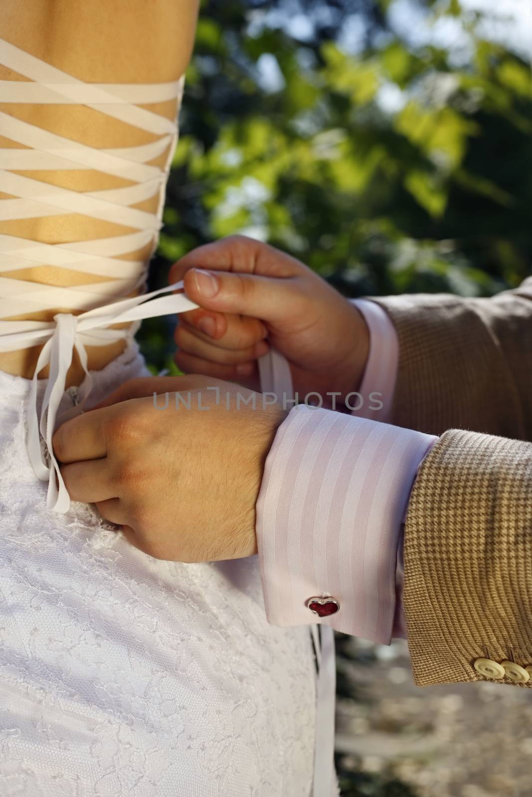 The groom helps the bride to tie a ribbon on the dress
