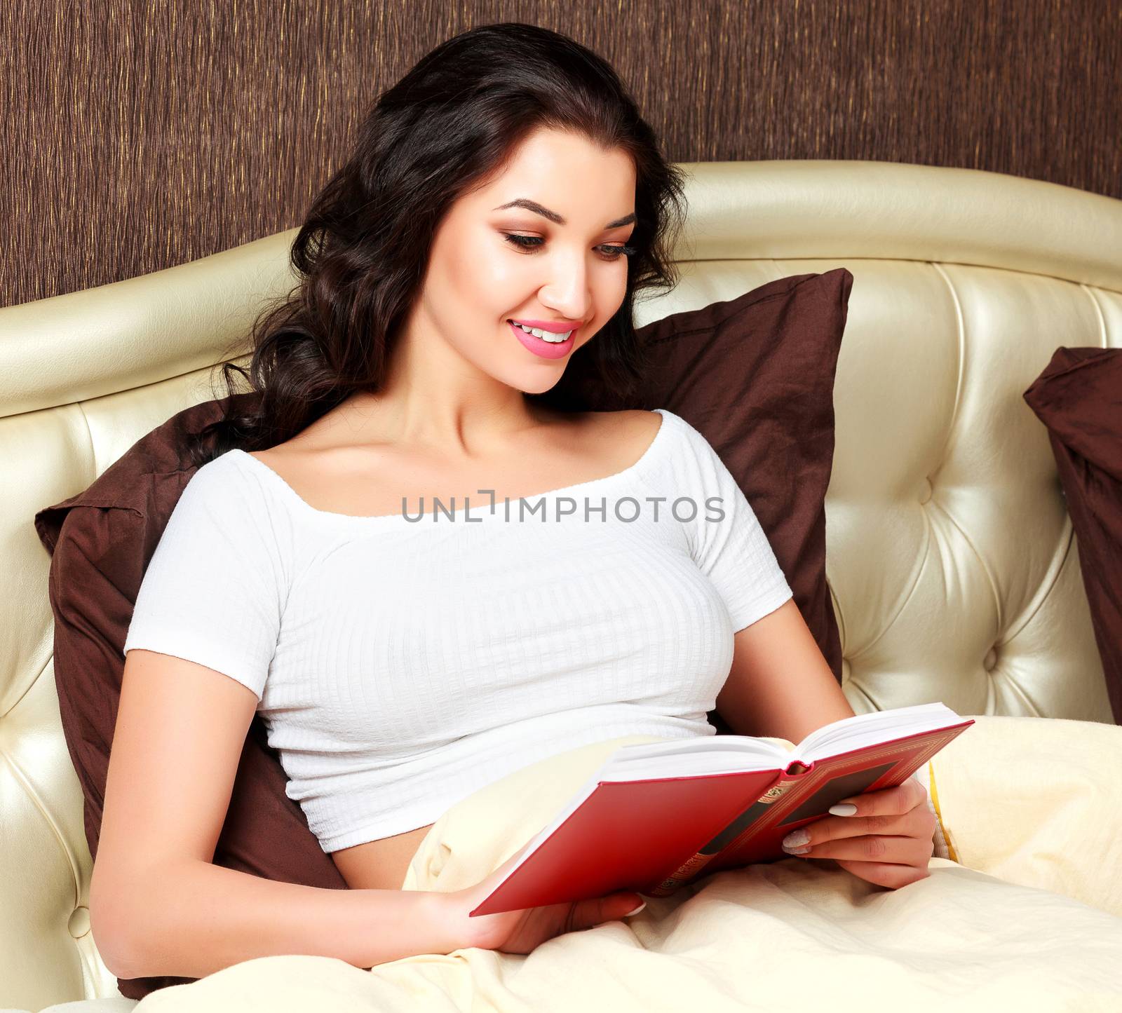 Young woman reading a book in bed by Nobilior