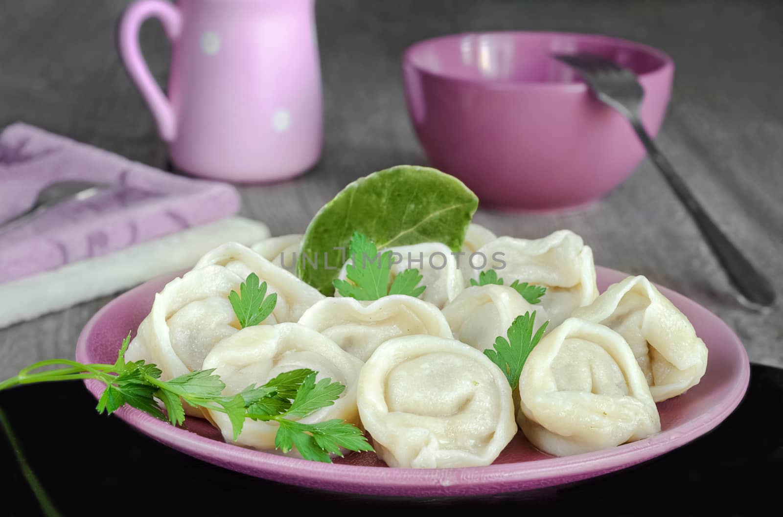 Meat dumplings on the plate and black surface. Kitchenware and gray wooden background. Selective focus.