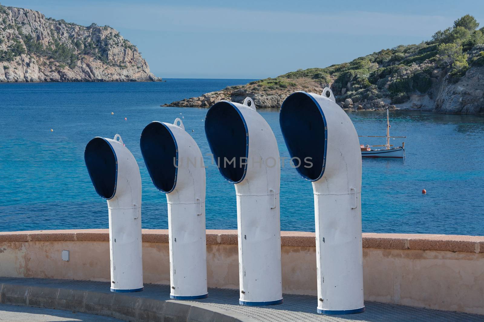 Boat ventilation or ventilation pipes on a street. In the background, the blue Mediterranean with fishing boat.