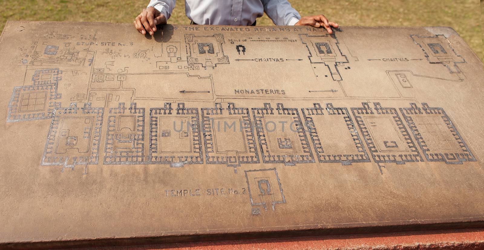 Archaeological heritage of India, ruins of university of Nalanda. Stone with the scheme of excavation. The hands of the Indian guide and plan of territory.      