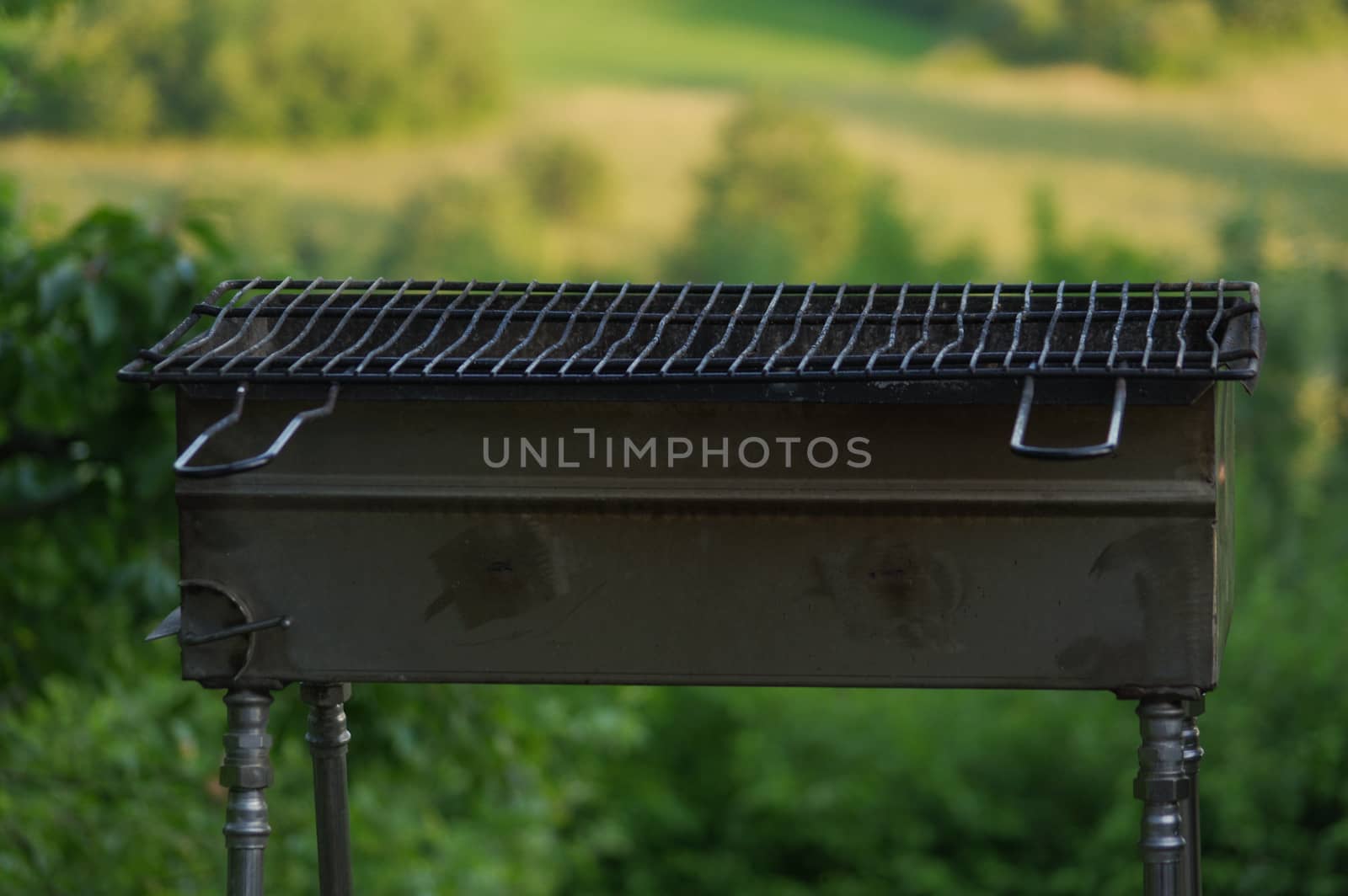 a empty portable BBQ grill in front of a fresh green summer landscape