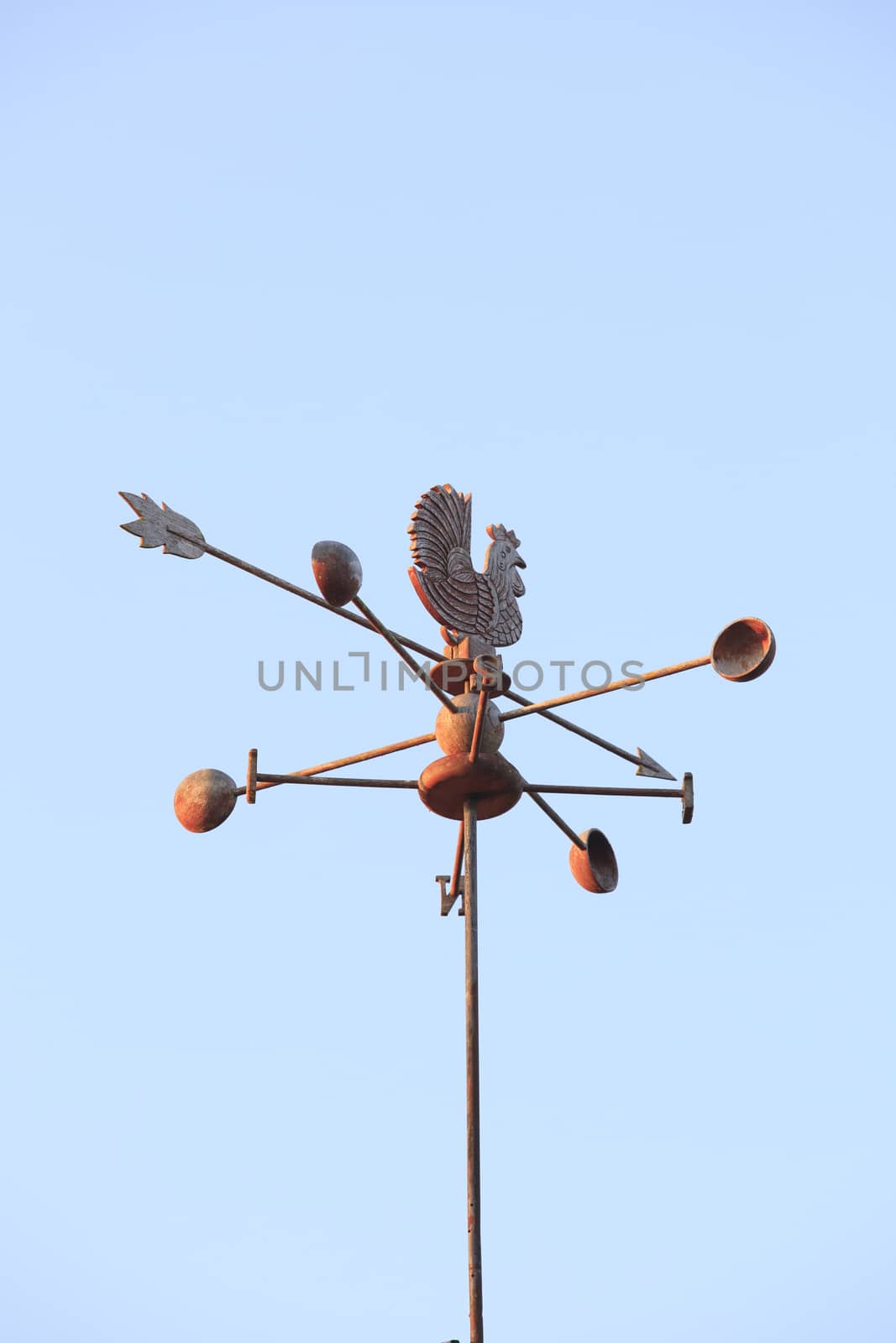 Weather Vane compass over house roof against blue sky background with copy space