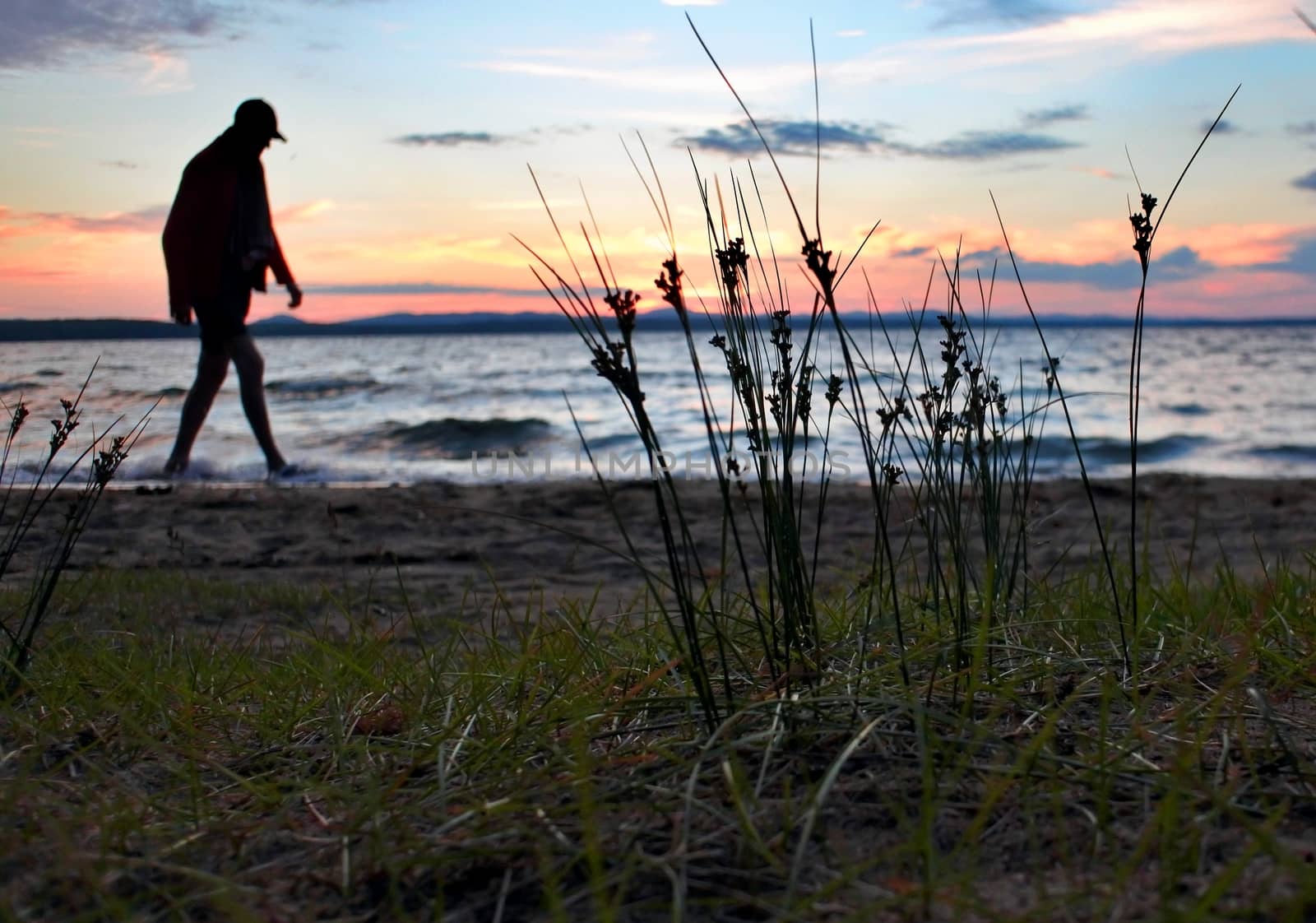 a lone man walking on the shore of the lake in the evening