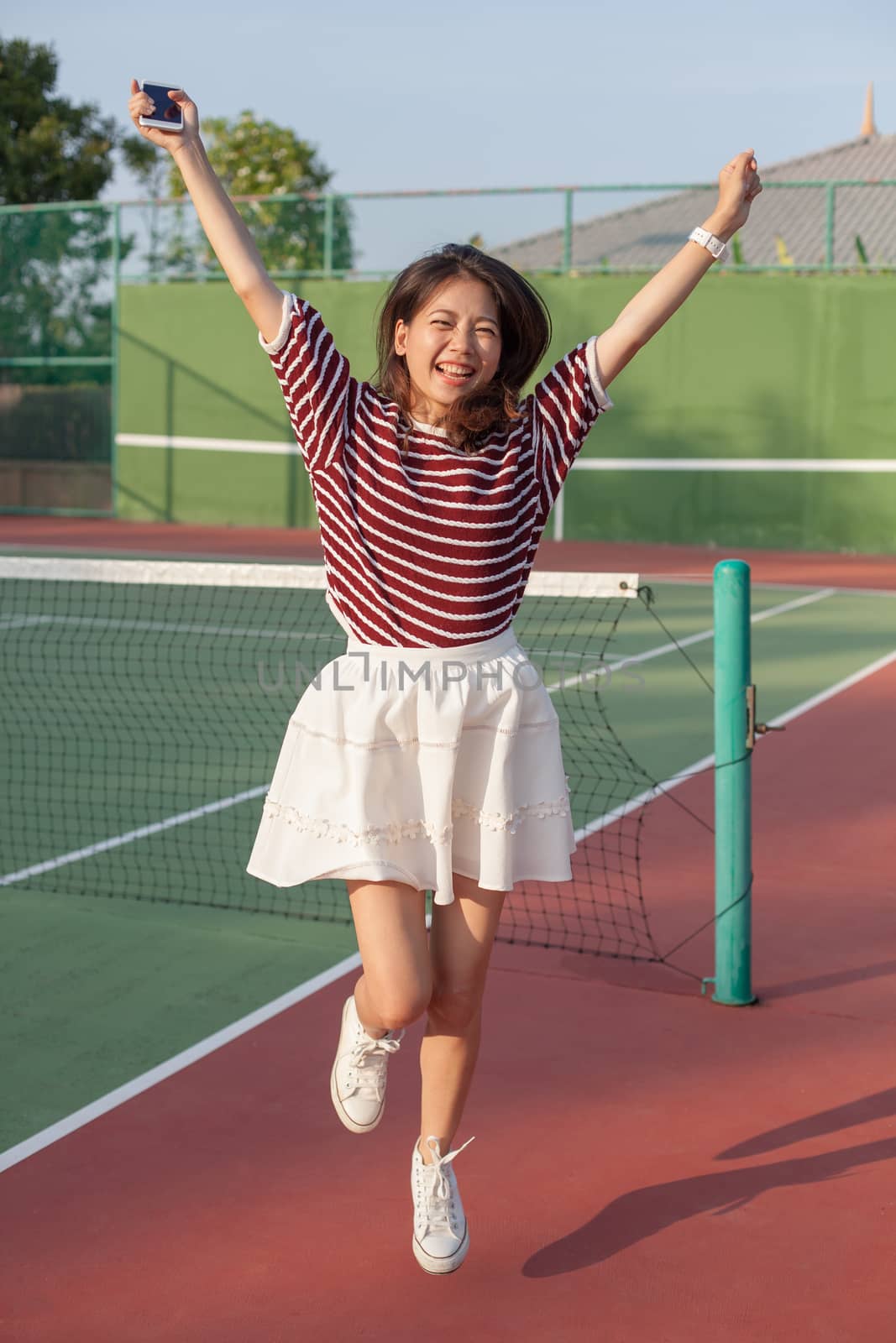 asian woman in sport tennis course jumping with happiness emotio by khunaspix