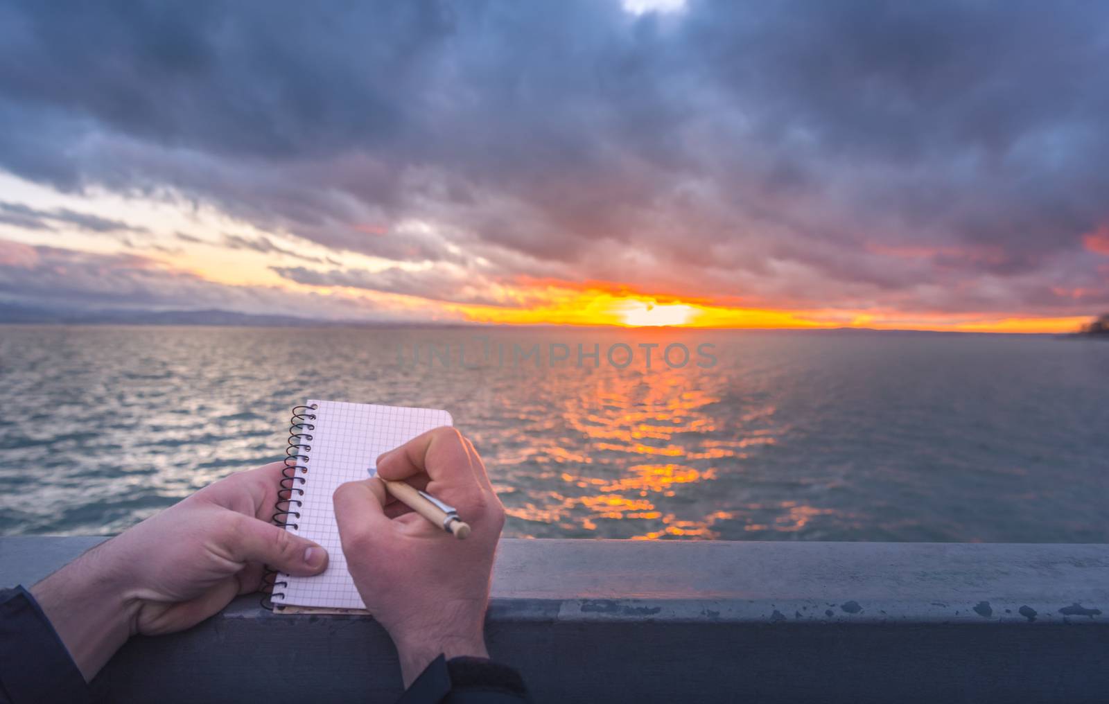 Writing on a notebook at sunset by YesPhotographers