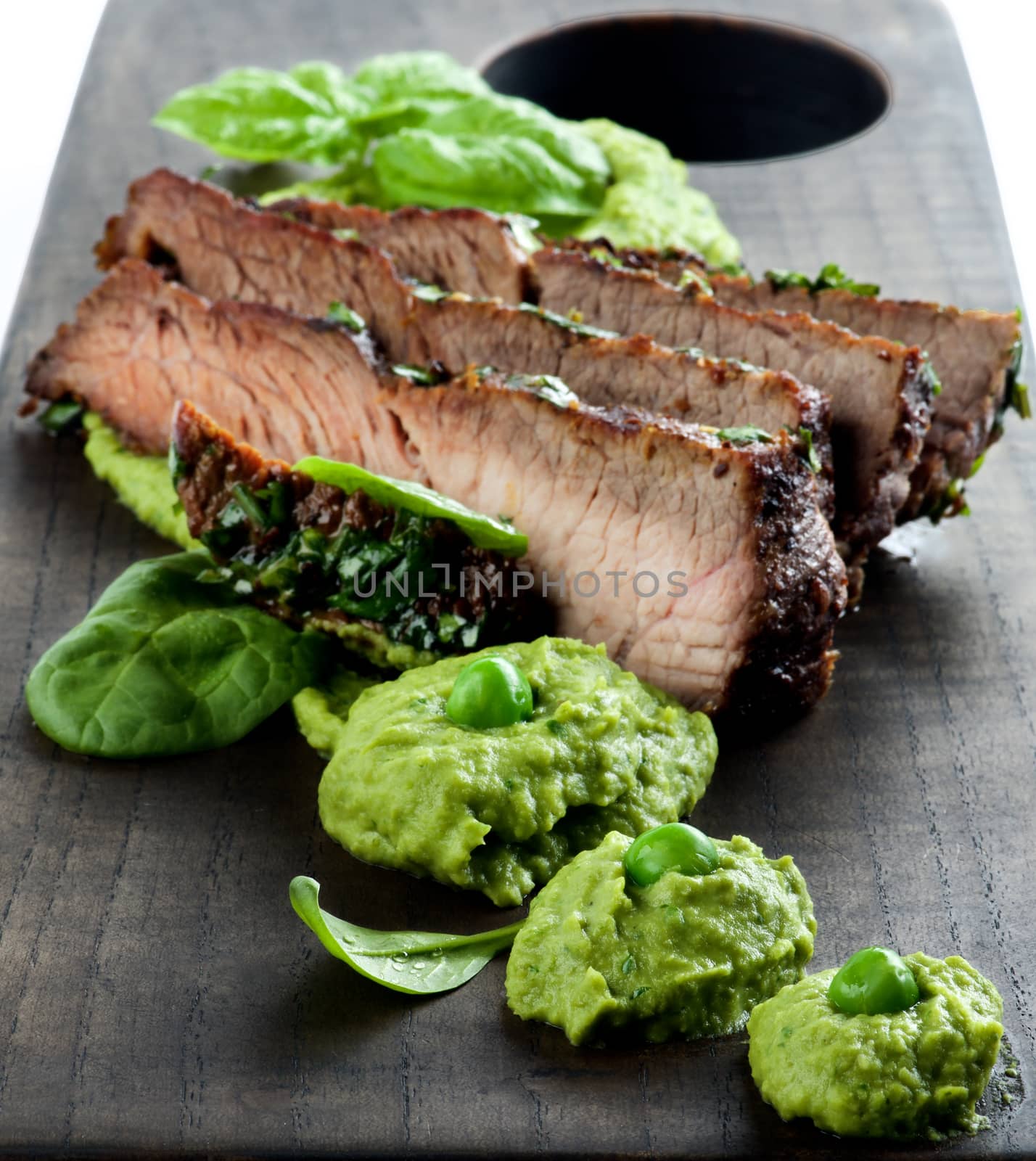 Delicious Roasted in Herbs Pork and Mashed Green Pea Puree on Wooden Serving Board closeup. Focus on Foreground