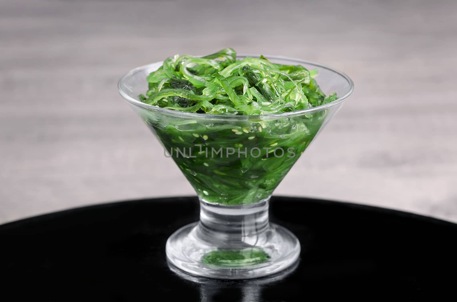 Seaweed in a glass vase, on a black surface and grey background. Selective focus.