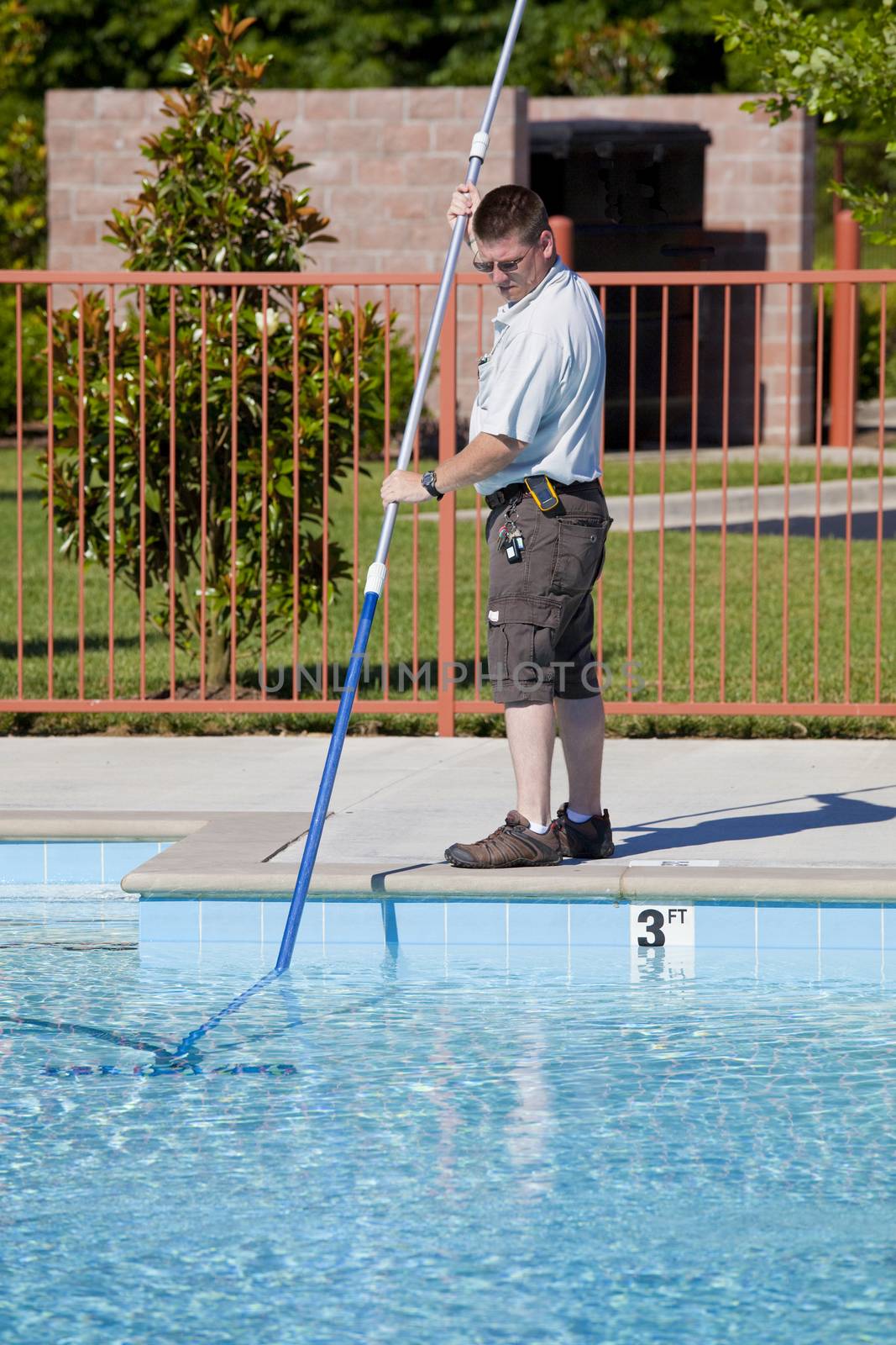 Service man checking chlorine, PH and other chemical levels and cleaning community pool