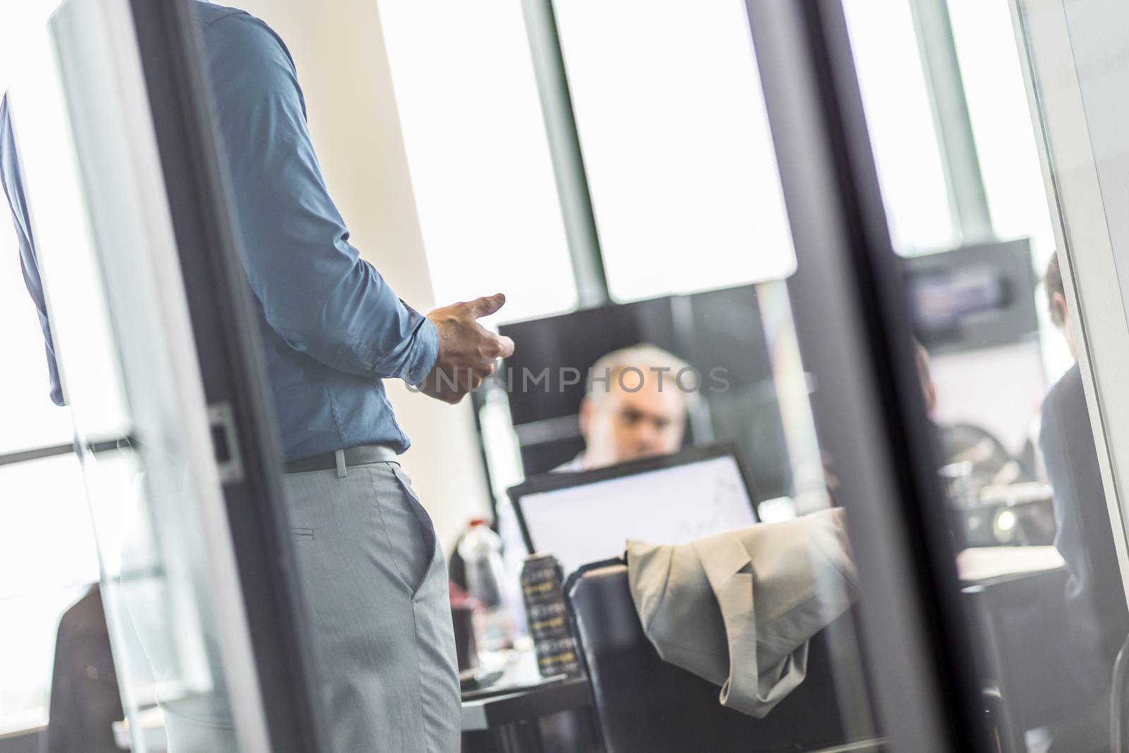 Business man making a presentation at office. Business executive delivering a presentation to his colleagues during meeting or business training. View through glass. Business and entrepreneurship.