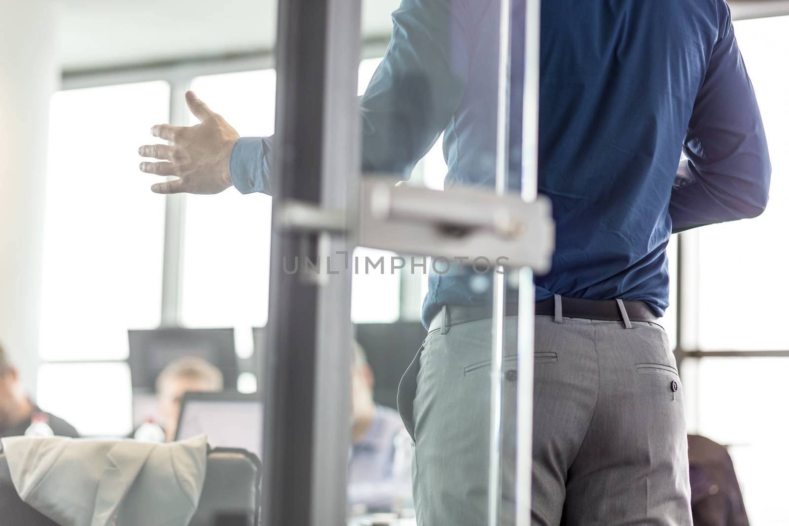 Business man making a presentation at office. Business executive delivering a presentation to his colleagues during meeting or business training. View through glass. Business and entrepreneurship.