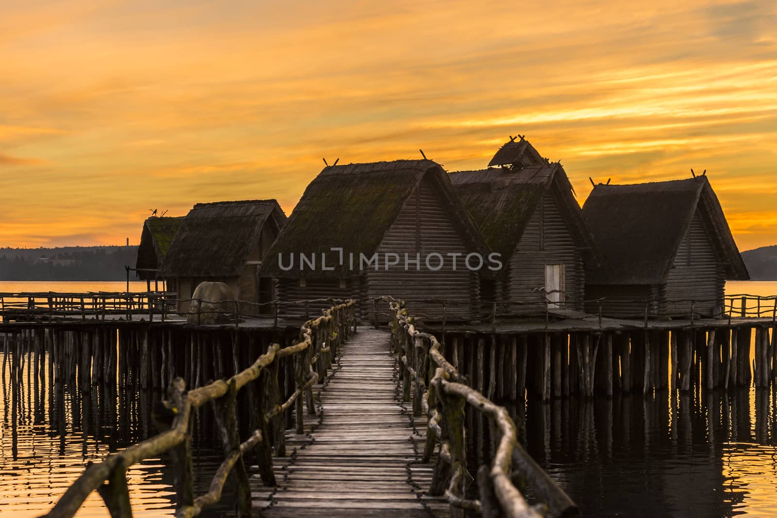 Wooden bridge and houses suspended over lake water by YesPhotographers