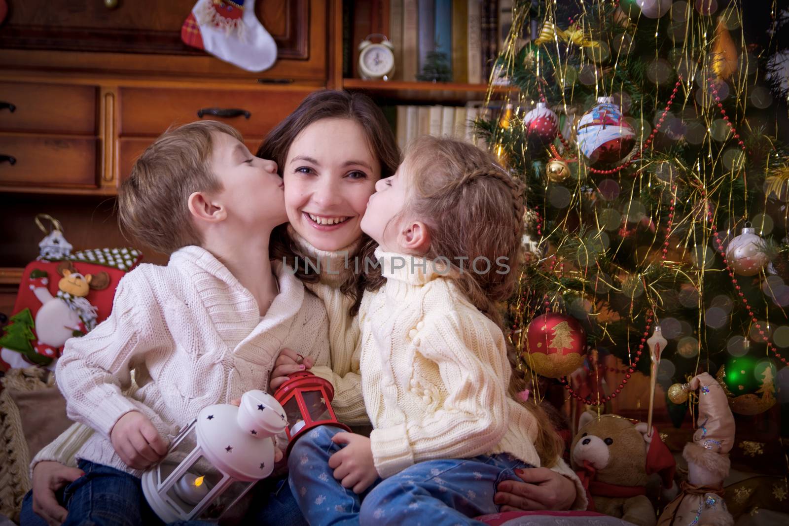 Two children kissing their mother under Christmas tree