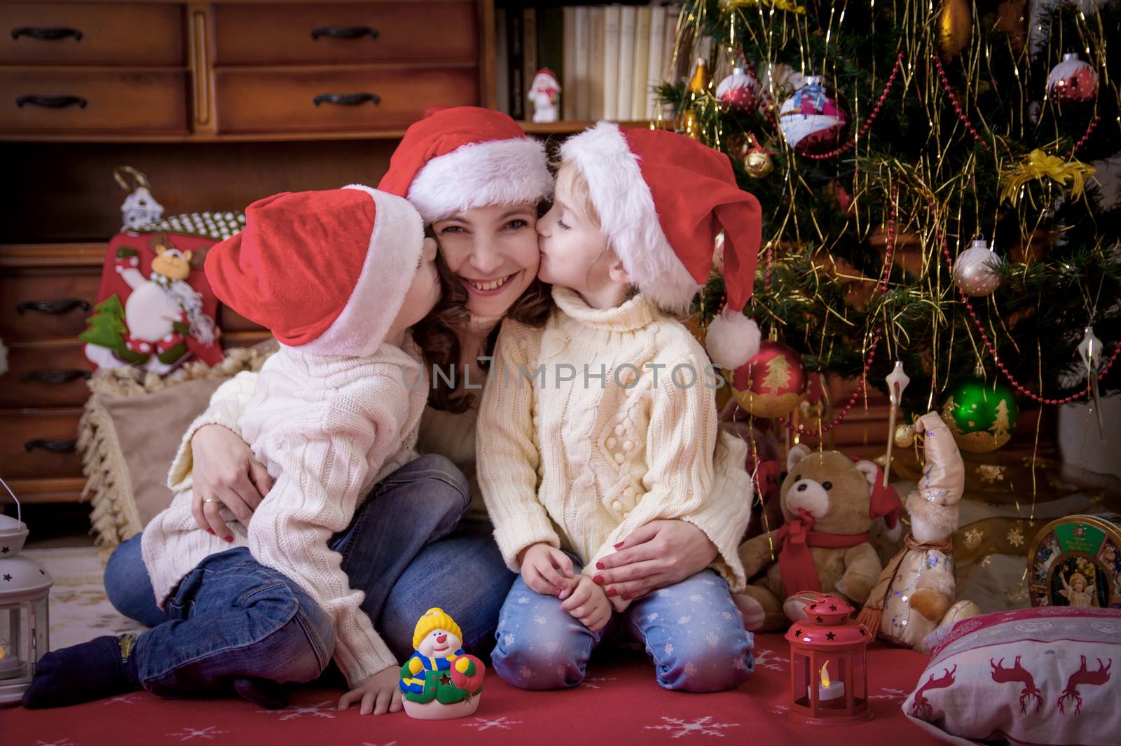 Kids kissing theit mother at cheek under Christmas tree by Angel_a