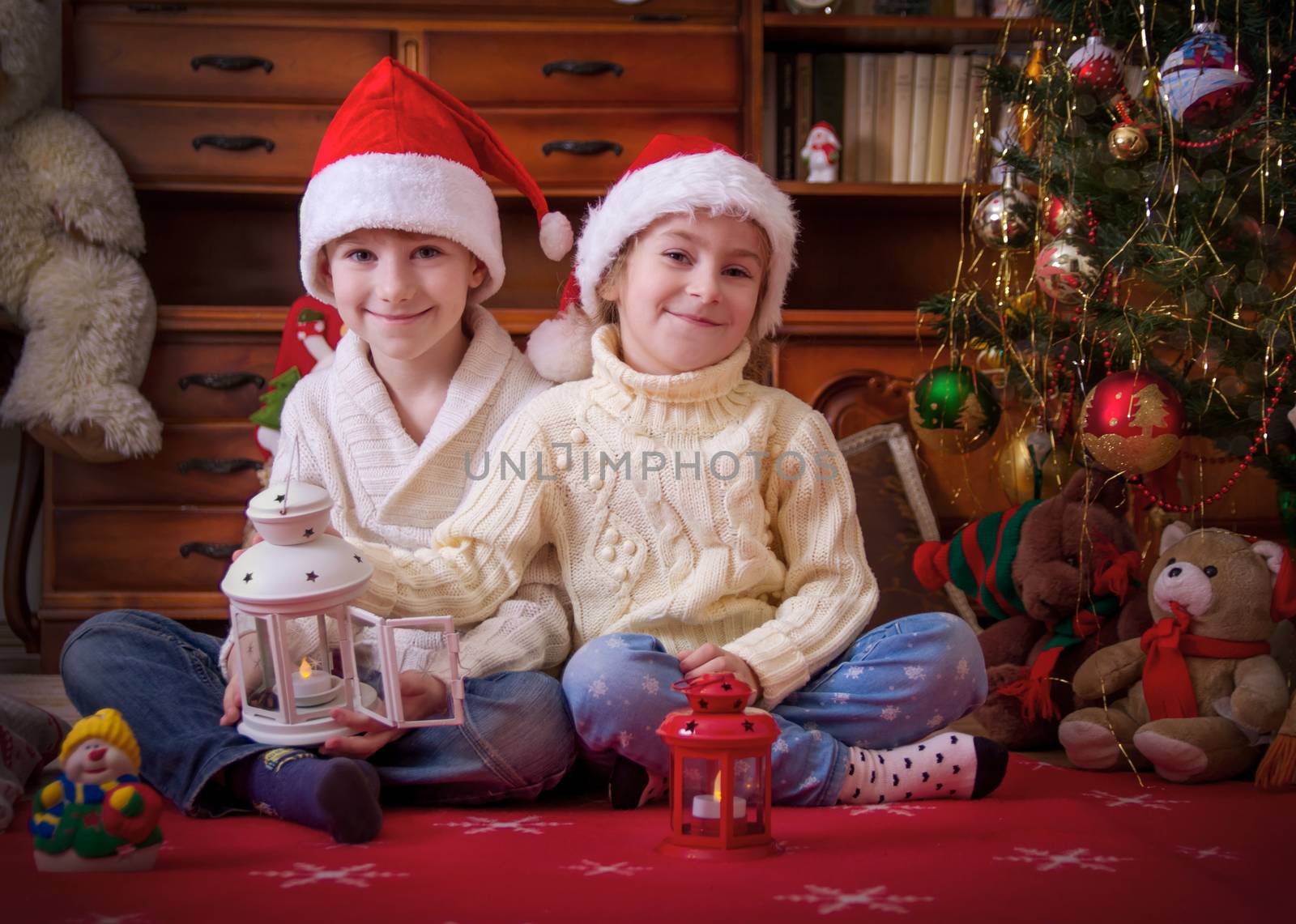 Two smiling kids playing with lanterns under Christmas tree