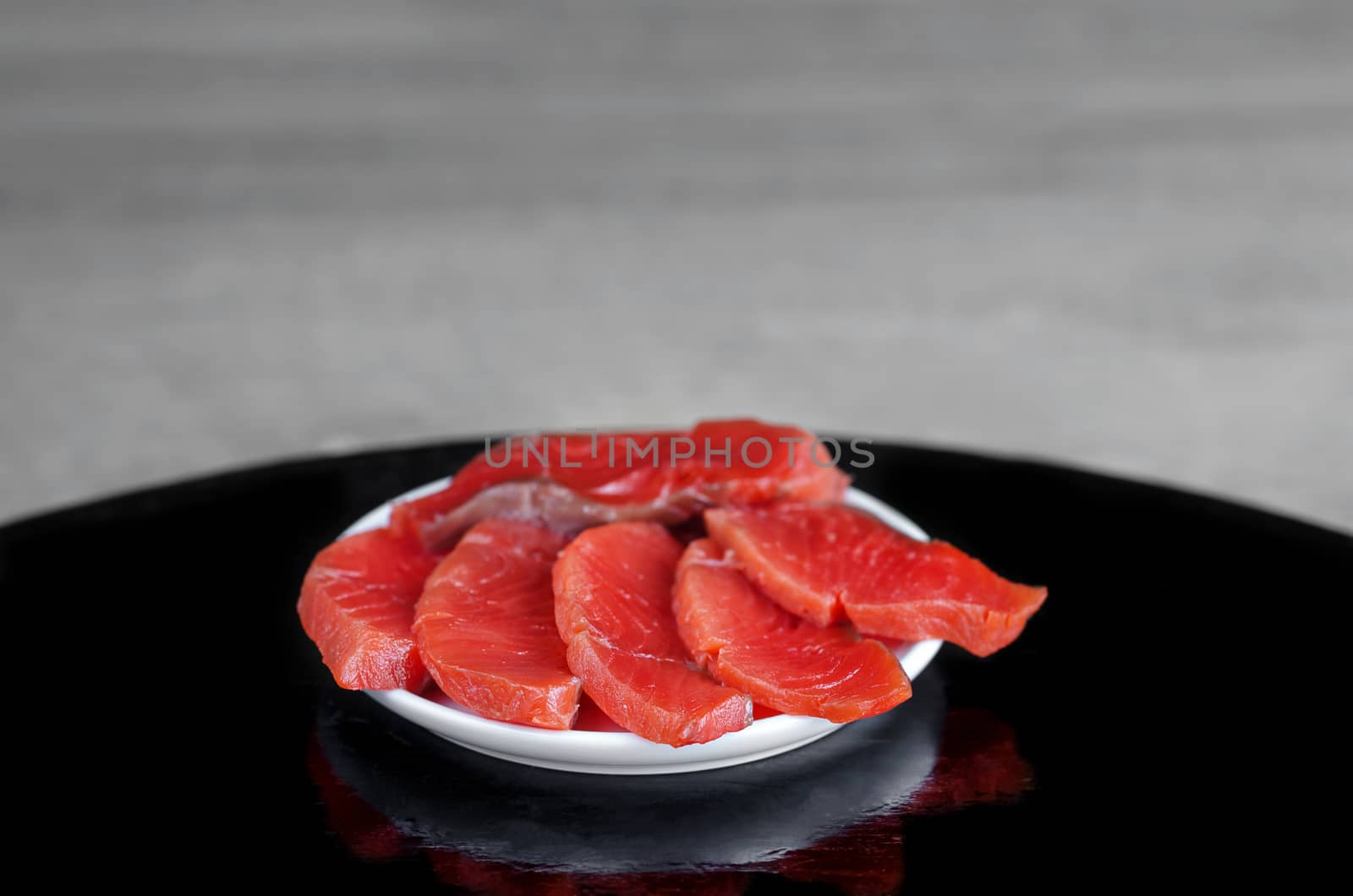 Red fish in a plate on the black wooden table and grey background. Selective focus.