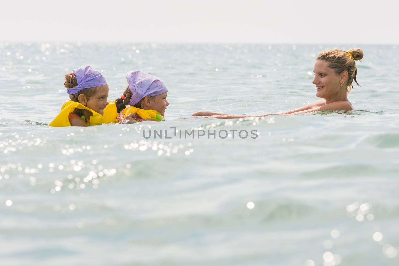 Mom floats in the sea with two small daughters in swimming vests
