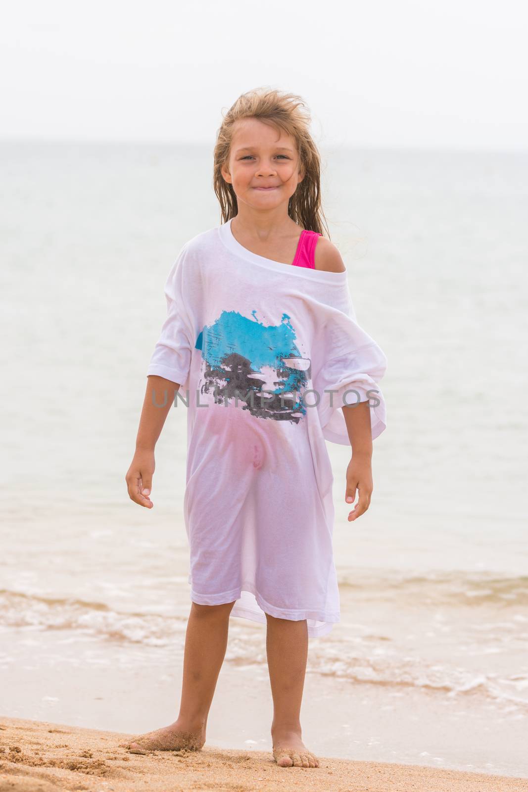 Cheerful girl basking on the beach wearing a large T-shirt parent