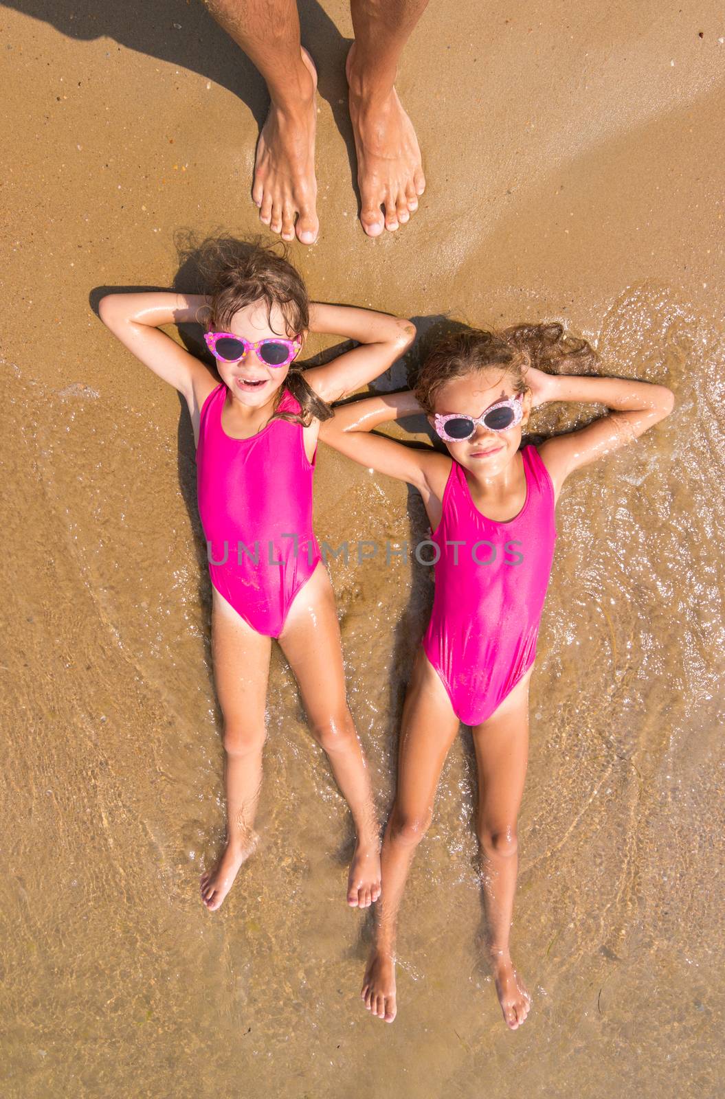 Two girls lie on his back on the surf of the sea sandy beach, there are a number of adult human foot