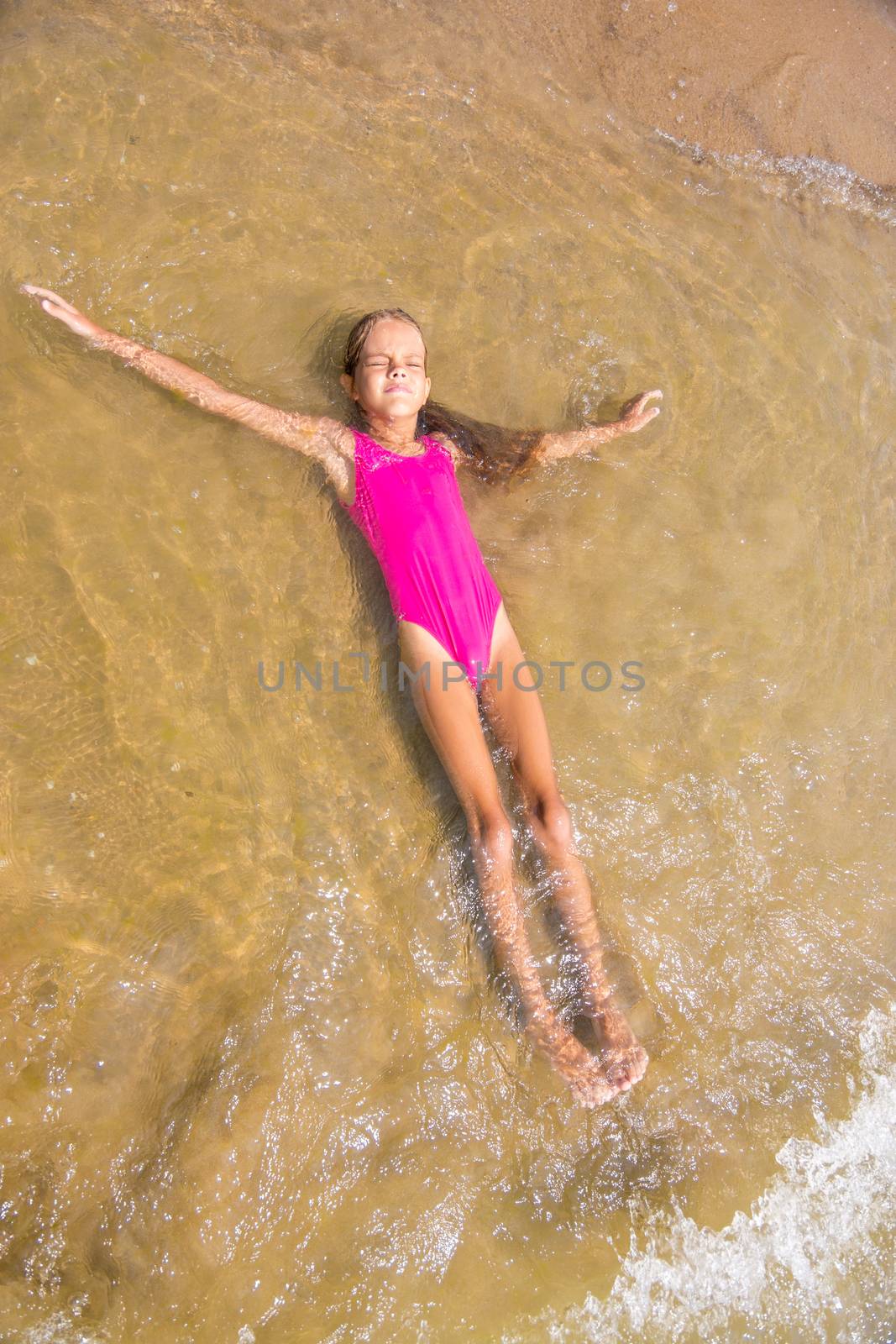 Seven-year girl lies on her back in the water on the sandy beach