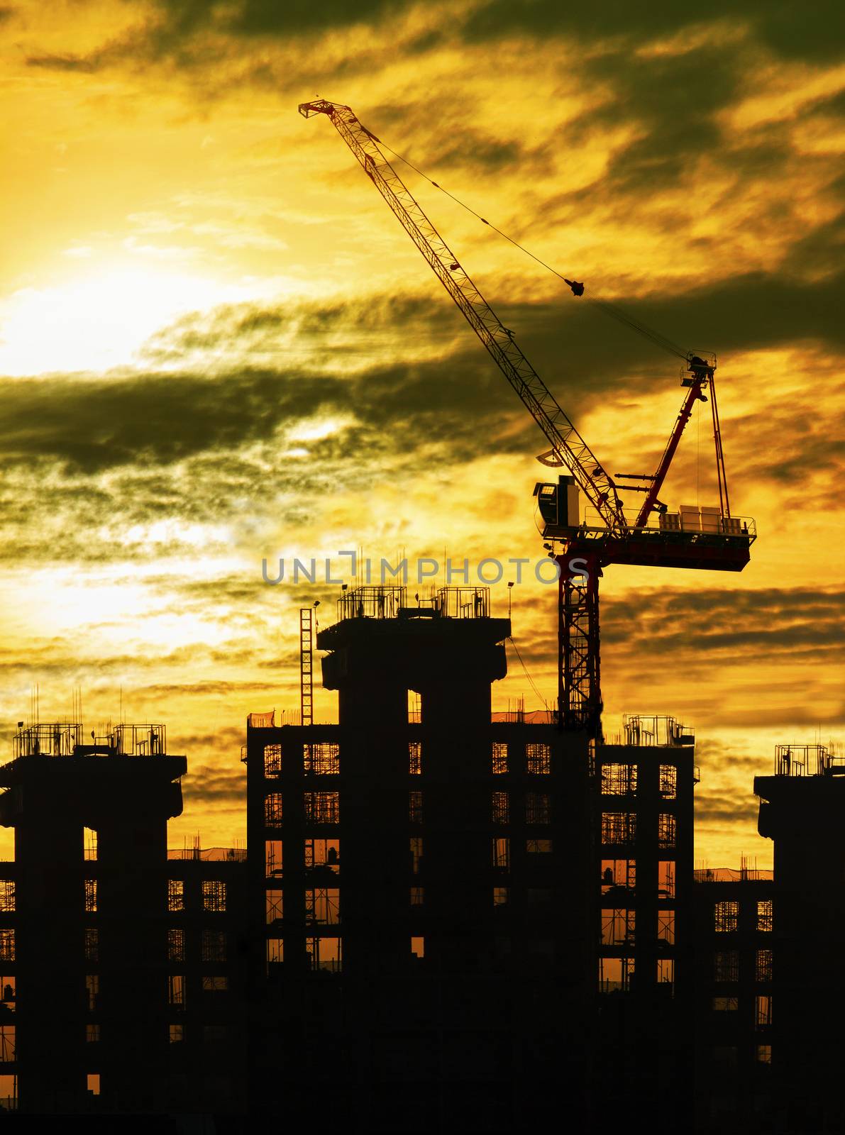 silhouette of crane and building construction and sun set sky wi by khunaspix