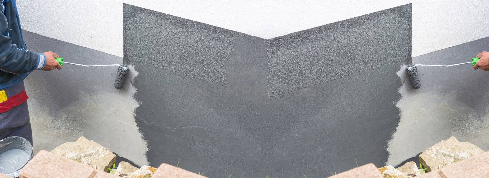 Close-up, arm of a house painter with paint roller in hand painting a house wall with gray paint.

