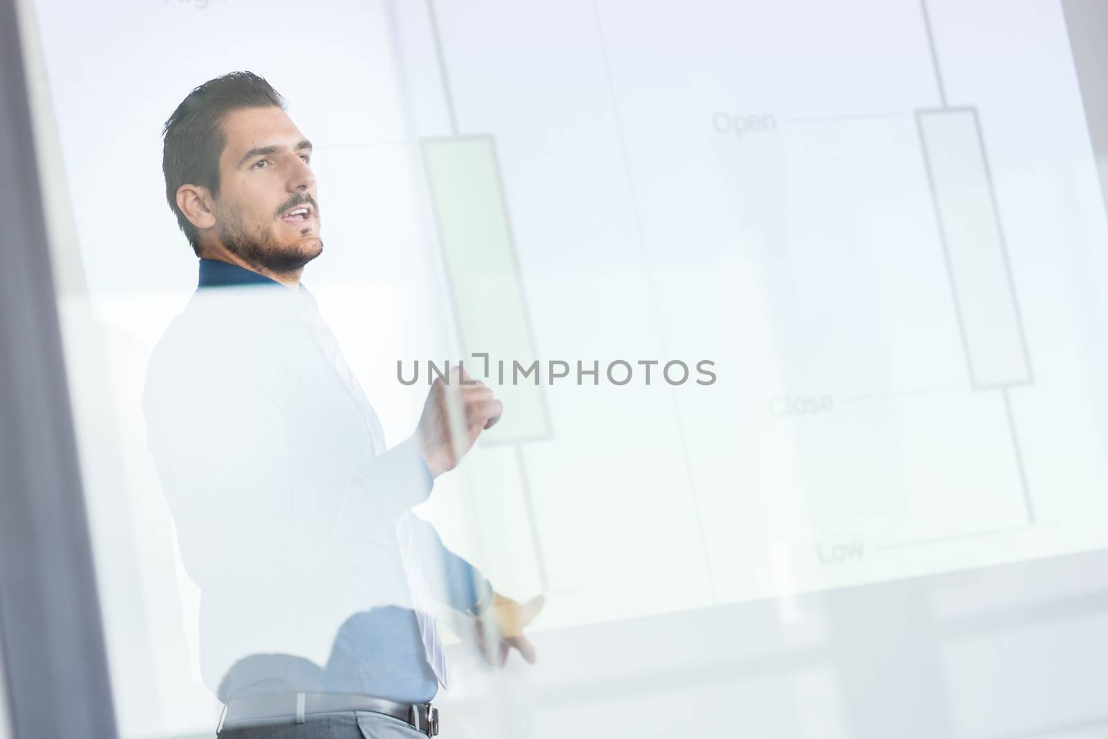 Business man making a presentation in front of whiteboard. Business executive delivering a presentation to his colleagues during meeting or in-house business training. View through glass.