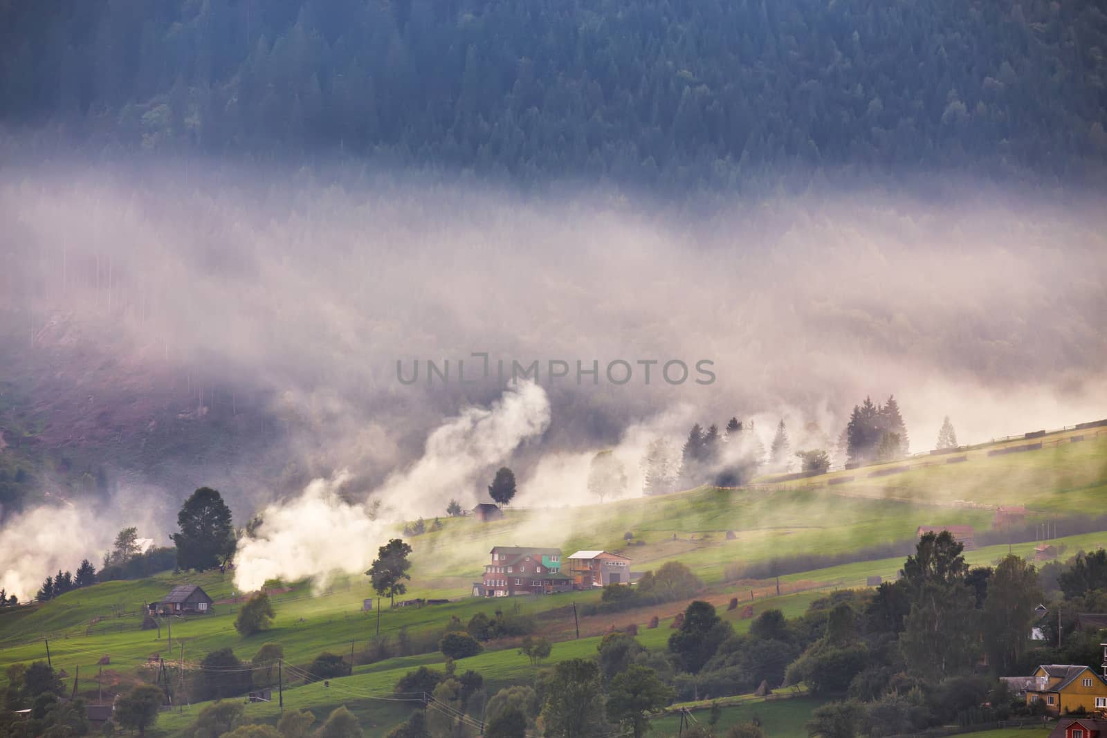 Alpine village in mountains. Smoke, bonfire and haze over hills by weise_maxim