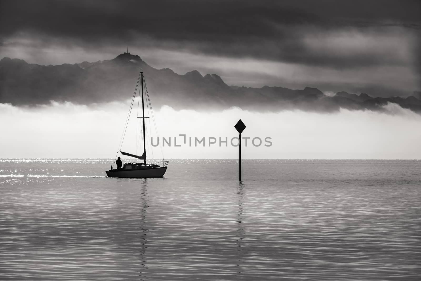 Black and white landscape with a boat sailing on the Bodensee lake, with mountains and morning mist at the horizon.