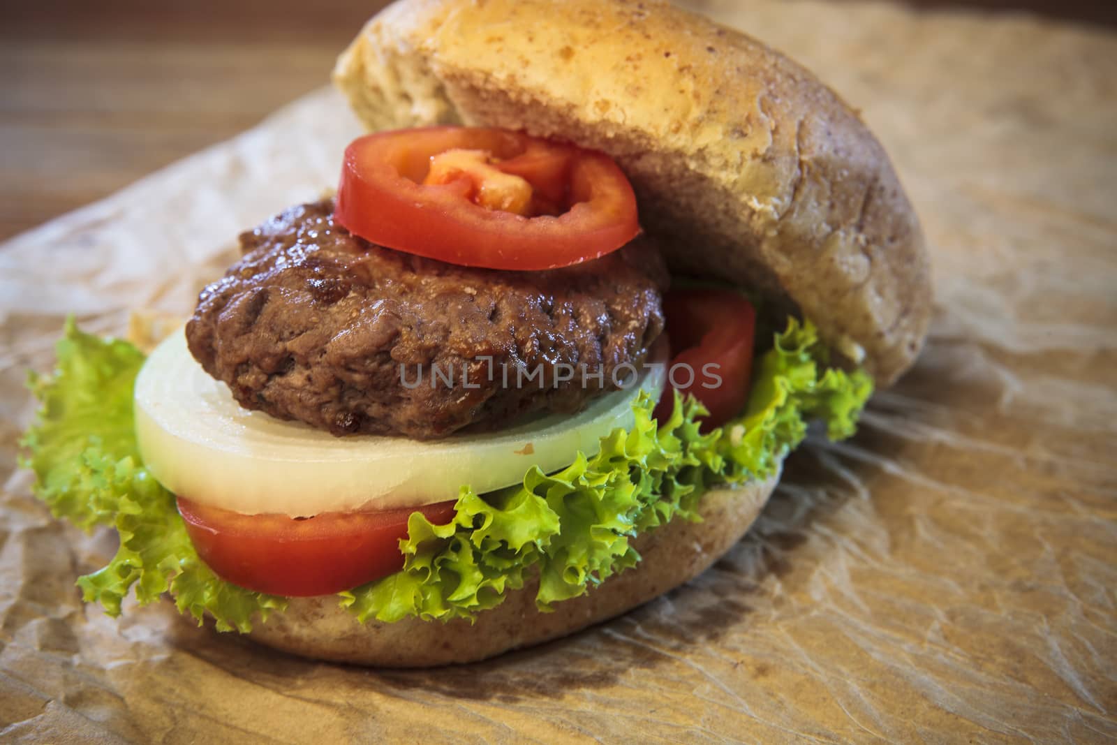 close up of ham burger and bun with tomatio onion and green vegetable on brown paper ready for meal eating