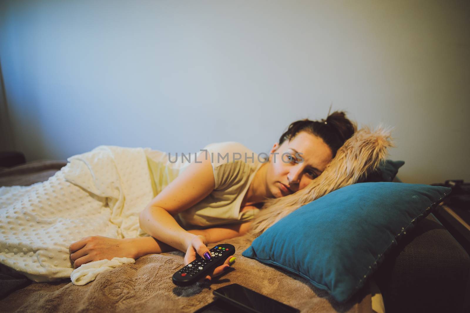 sick woman lying in bed with headache holding tv remote in hand