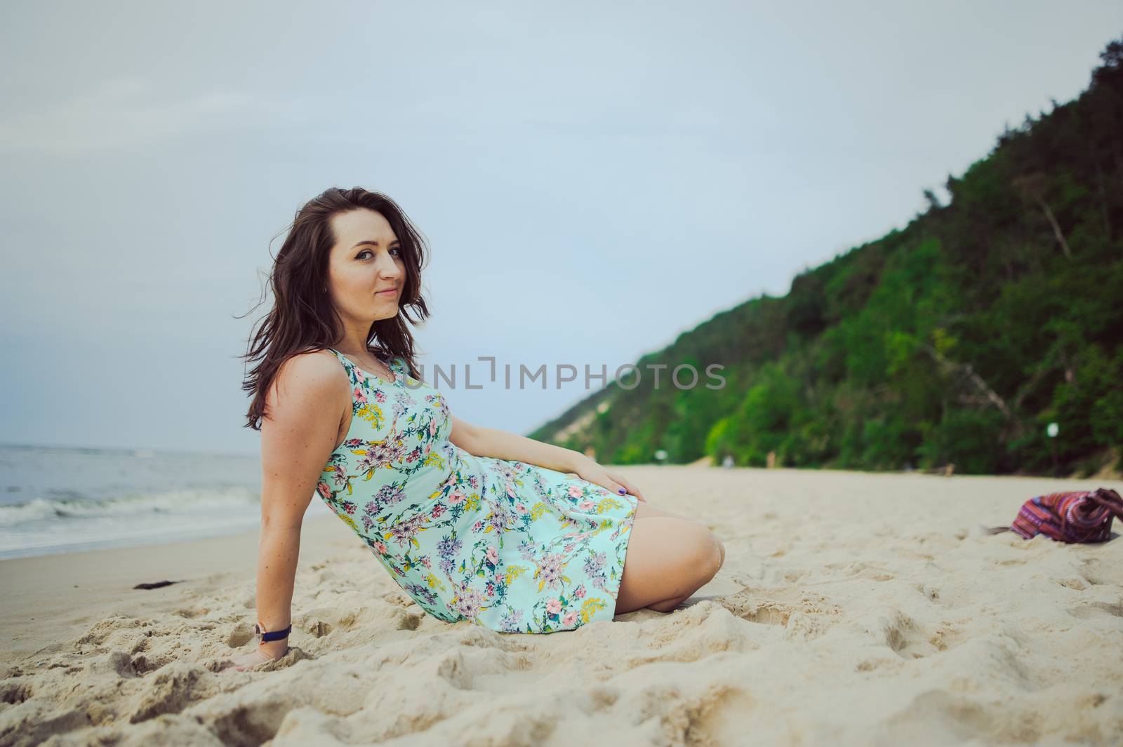 Young attractive brunette woman on a beach wearing dress
