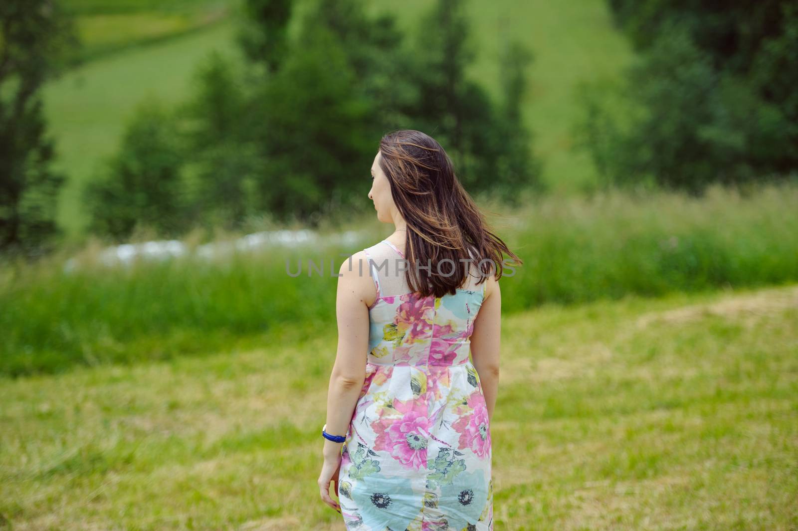 Brunette girl enjoying journey in mountains. Young smiling woman wearing dress traveling in countryside
