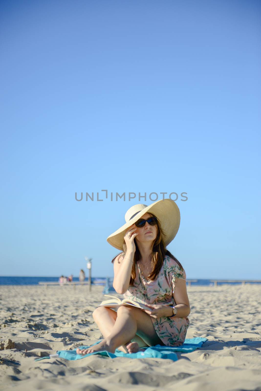 Portrait of a young brunette relaxing on the beach, reading a book. Summer time