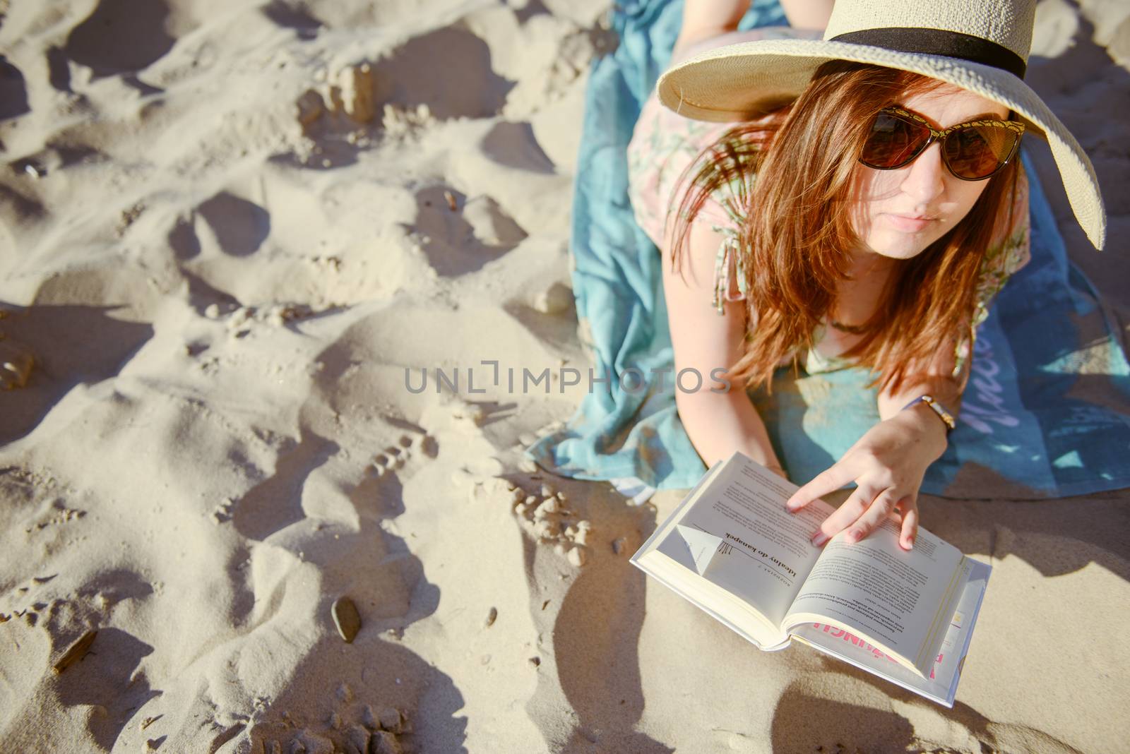 Portrait of a young brunette relaxing on the beach, reading a book. Summer time