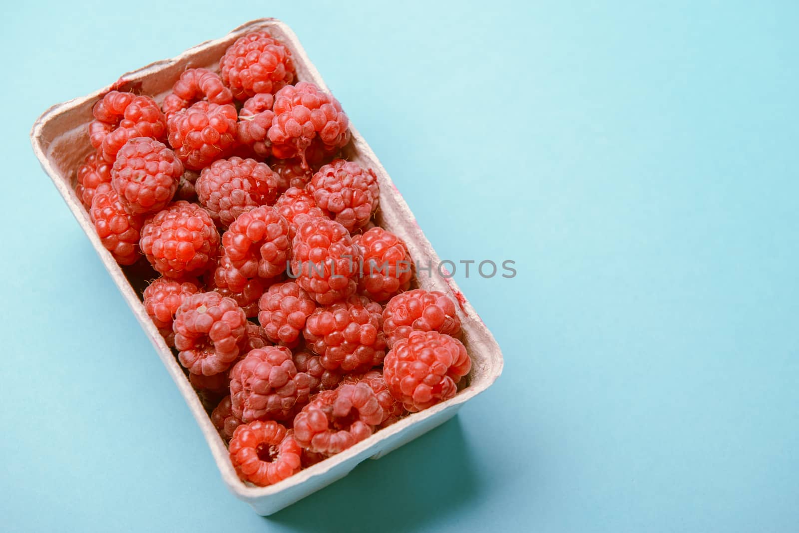 box of fresh raspberries on a blue background