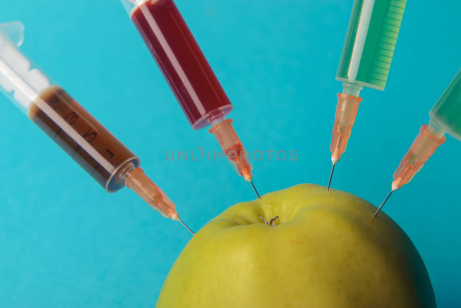 Chemical additives in food or genetically modified fruit concept. Green apple with syringes of chemicals. Isolated on blue background.