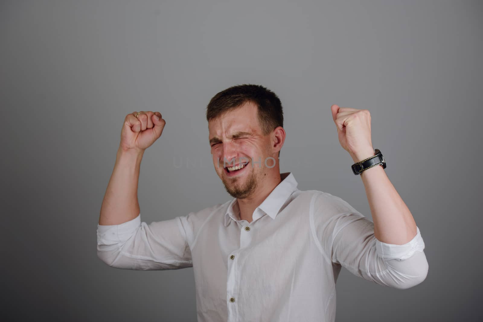 Young successful businessman standing with hands up and celebrating success. Gray background.