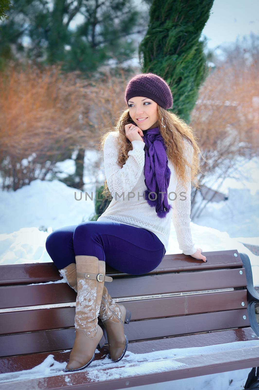 Young beautiful girl sitting on the bench in winter forest 