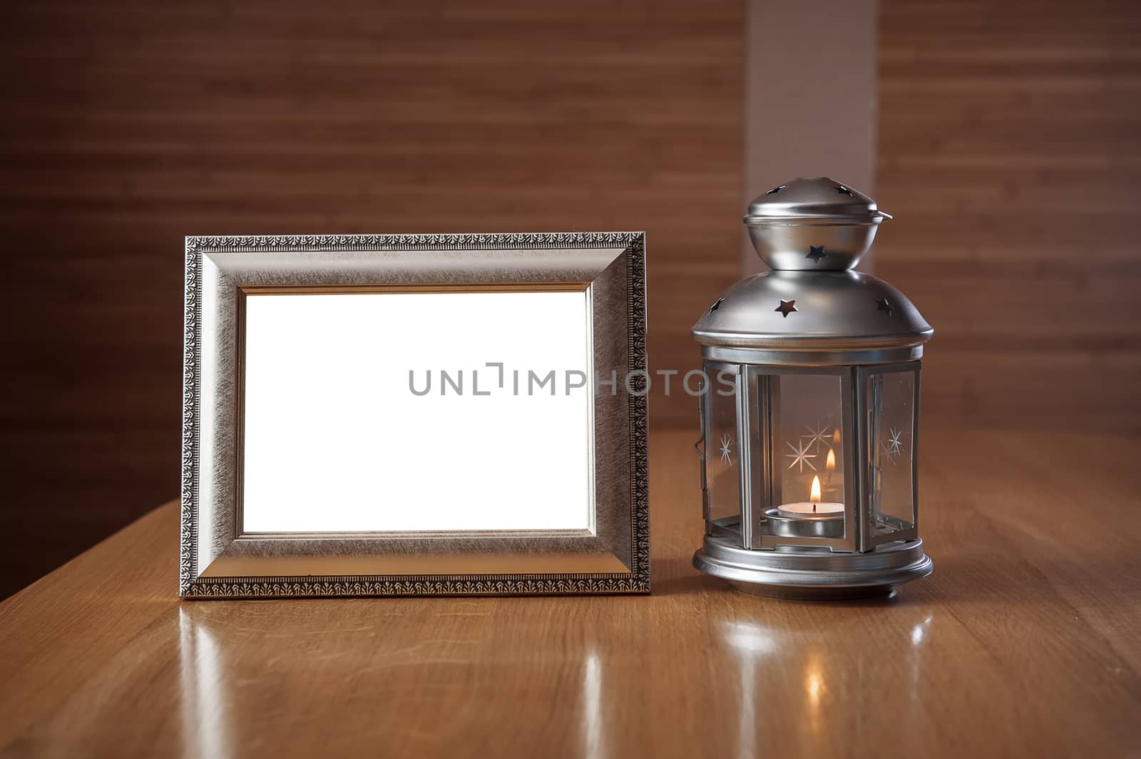 old photo frame on the wooden table against the background of a lantern with a candle