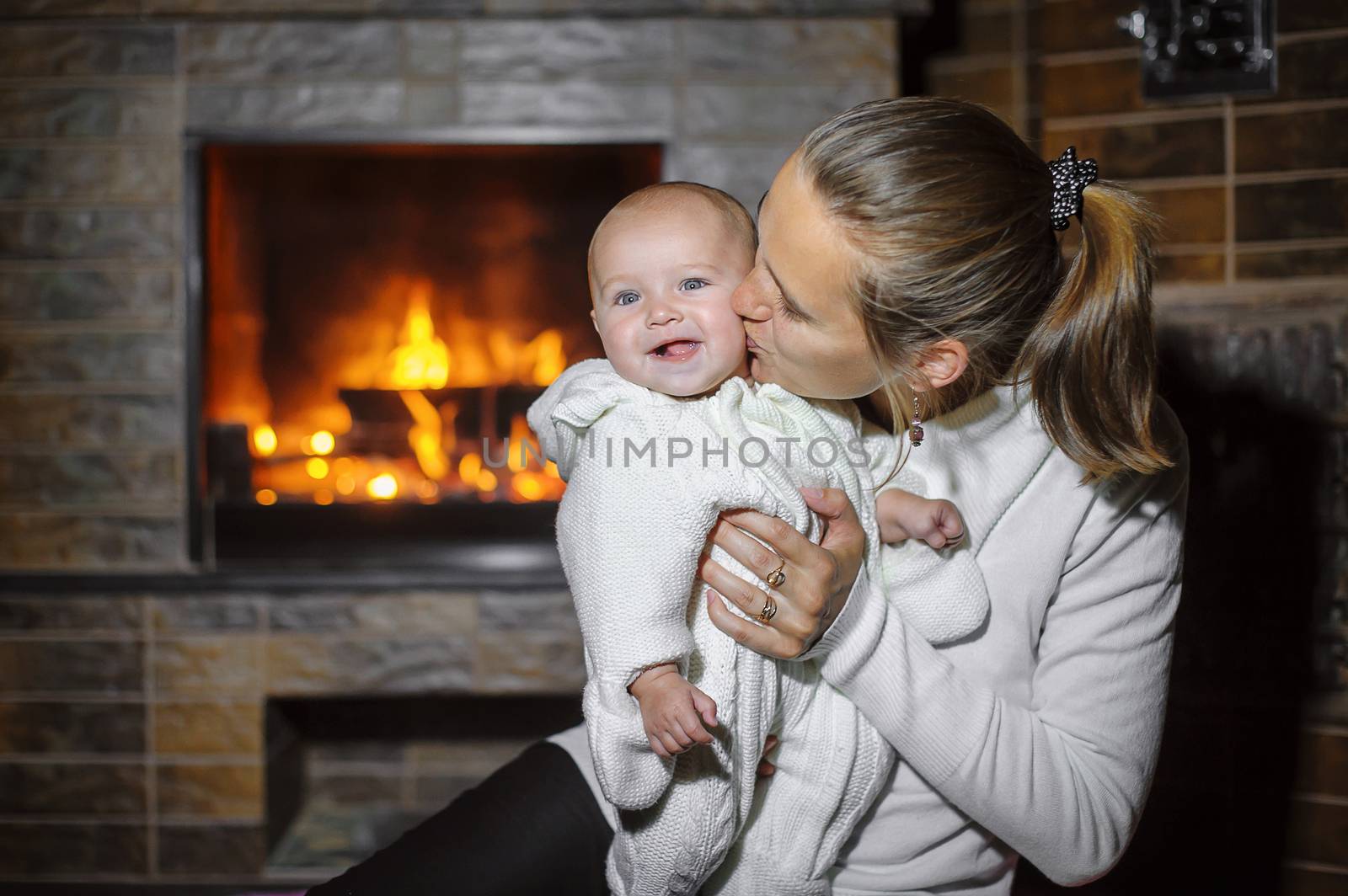 Mom kissing baby by the fireplace at home