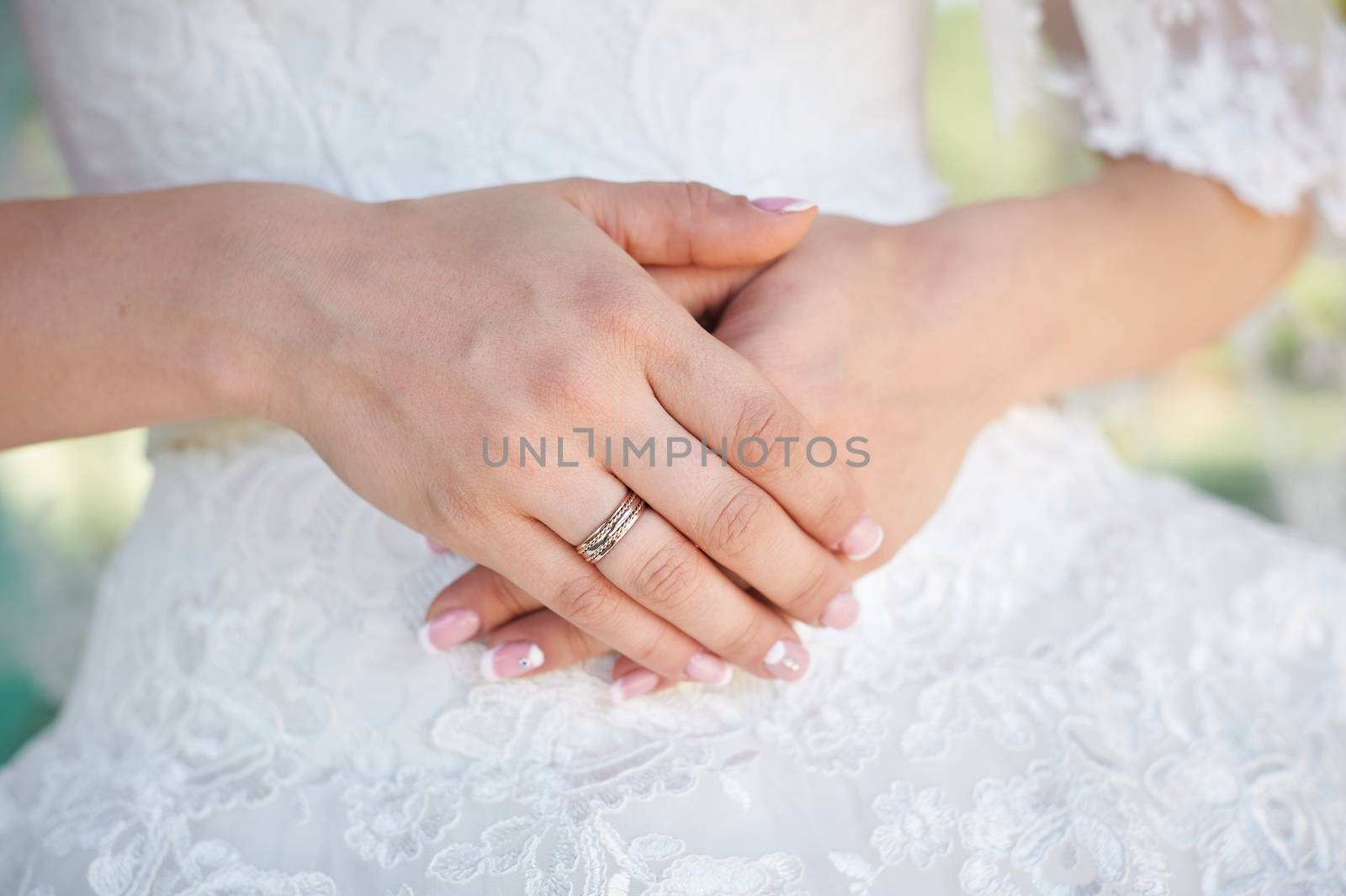 hands of the bride with a gold ring on a background of white dresses.
