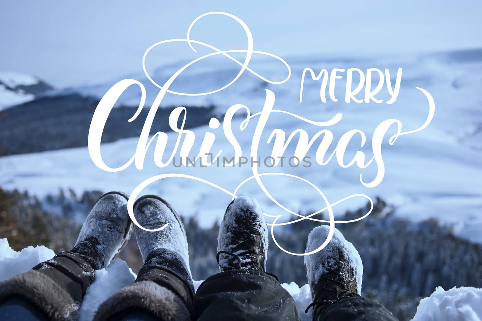 snow-covered feet of two hikers on a winter landscape with text Merry Christmas. Calligraphy lettering.