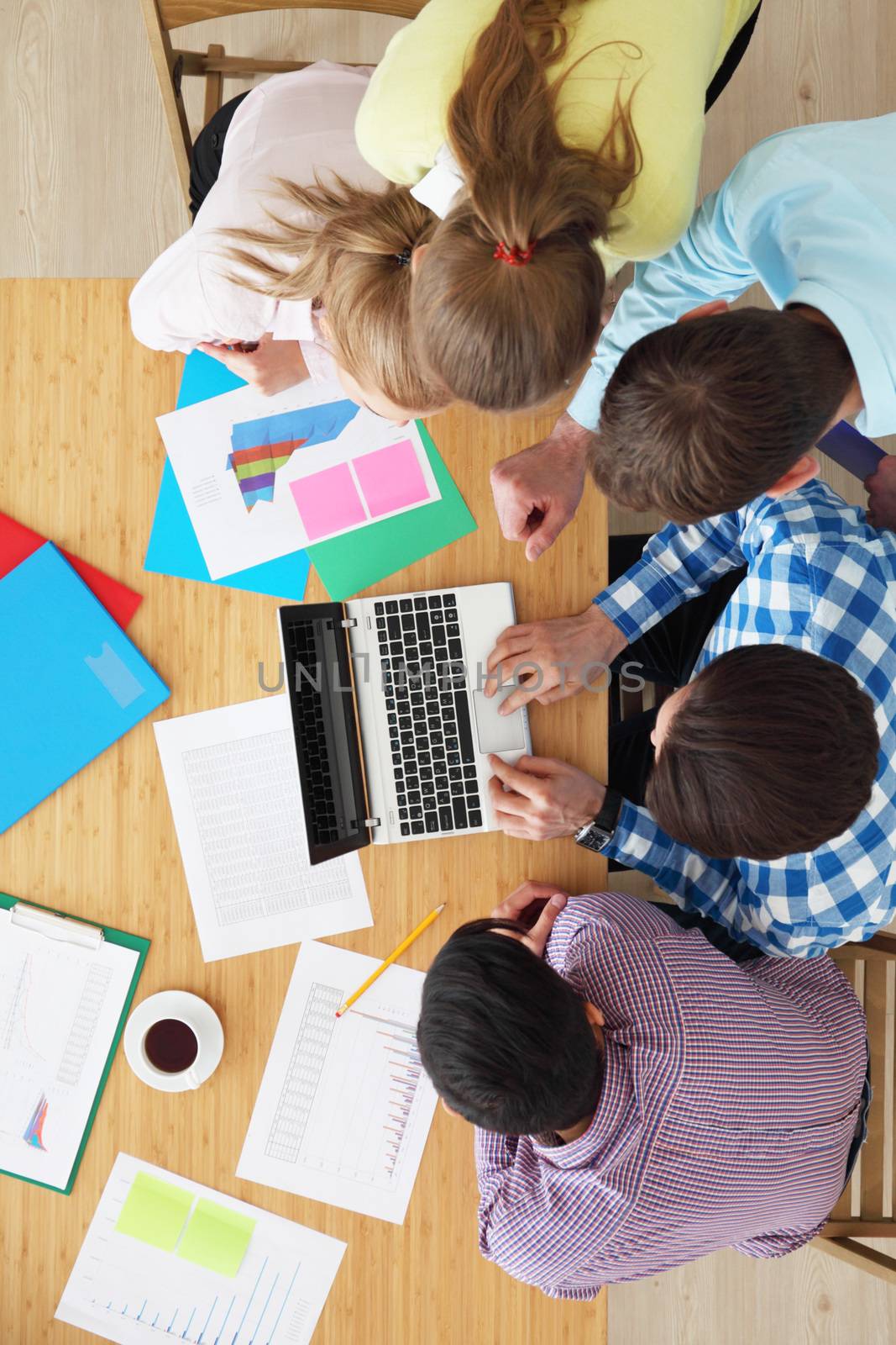 Businesspeople sitting at table looking at laptop screen, discussing financial documents with diagrams, top view