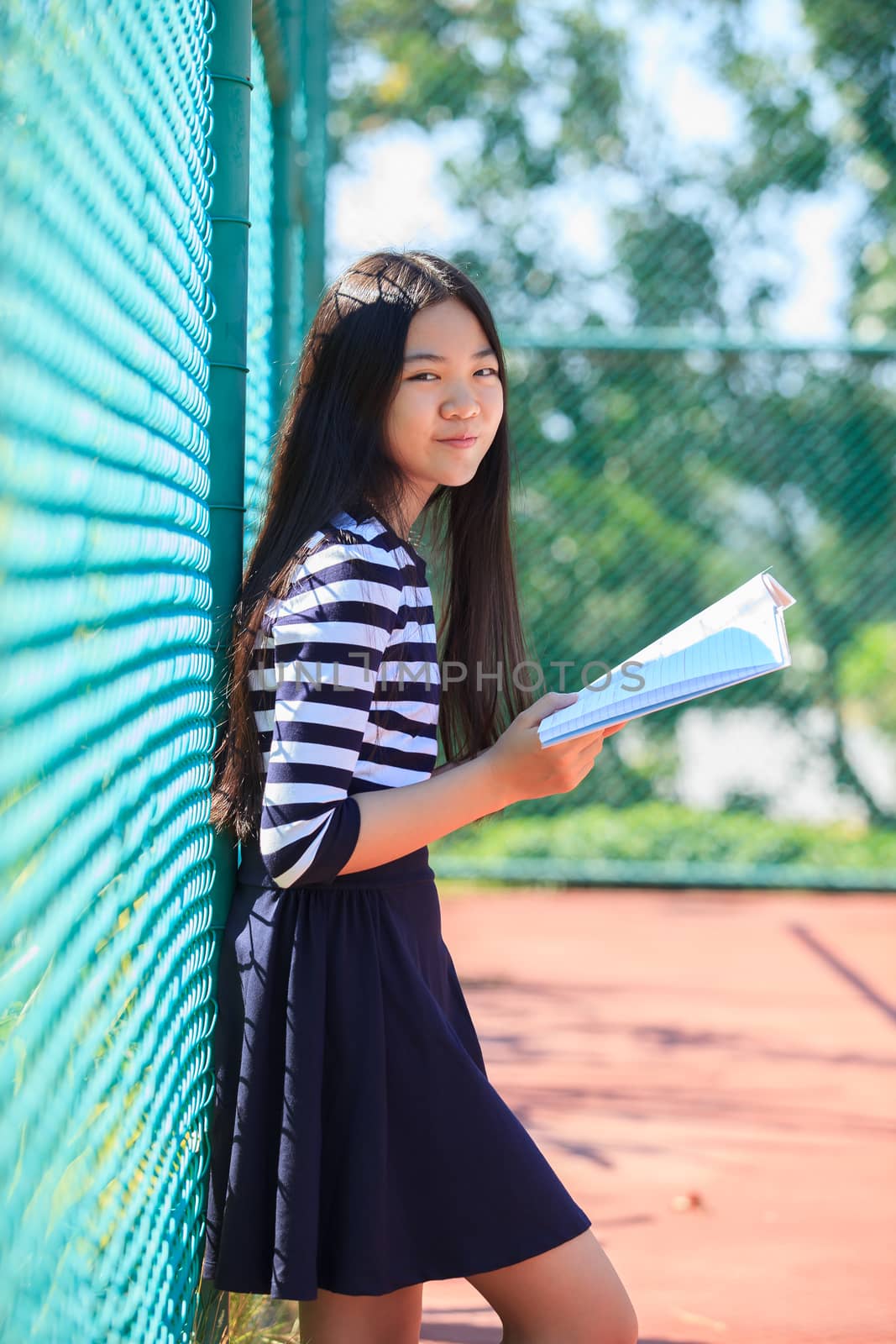 asian girl and school book in hand toothy smiling face with happiness emotion in green park