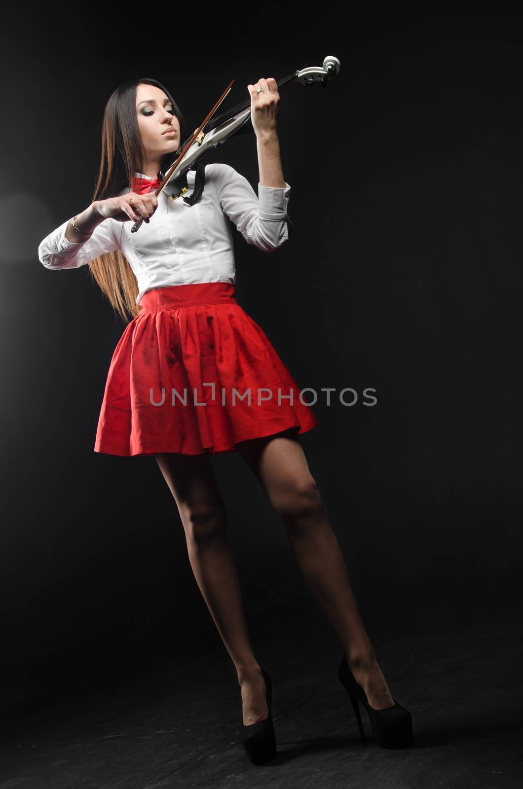 Pretty woman in a red skirt playing the violin on a black background