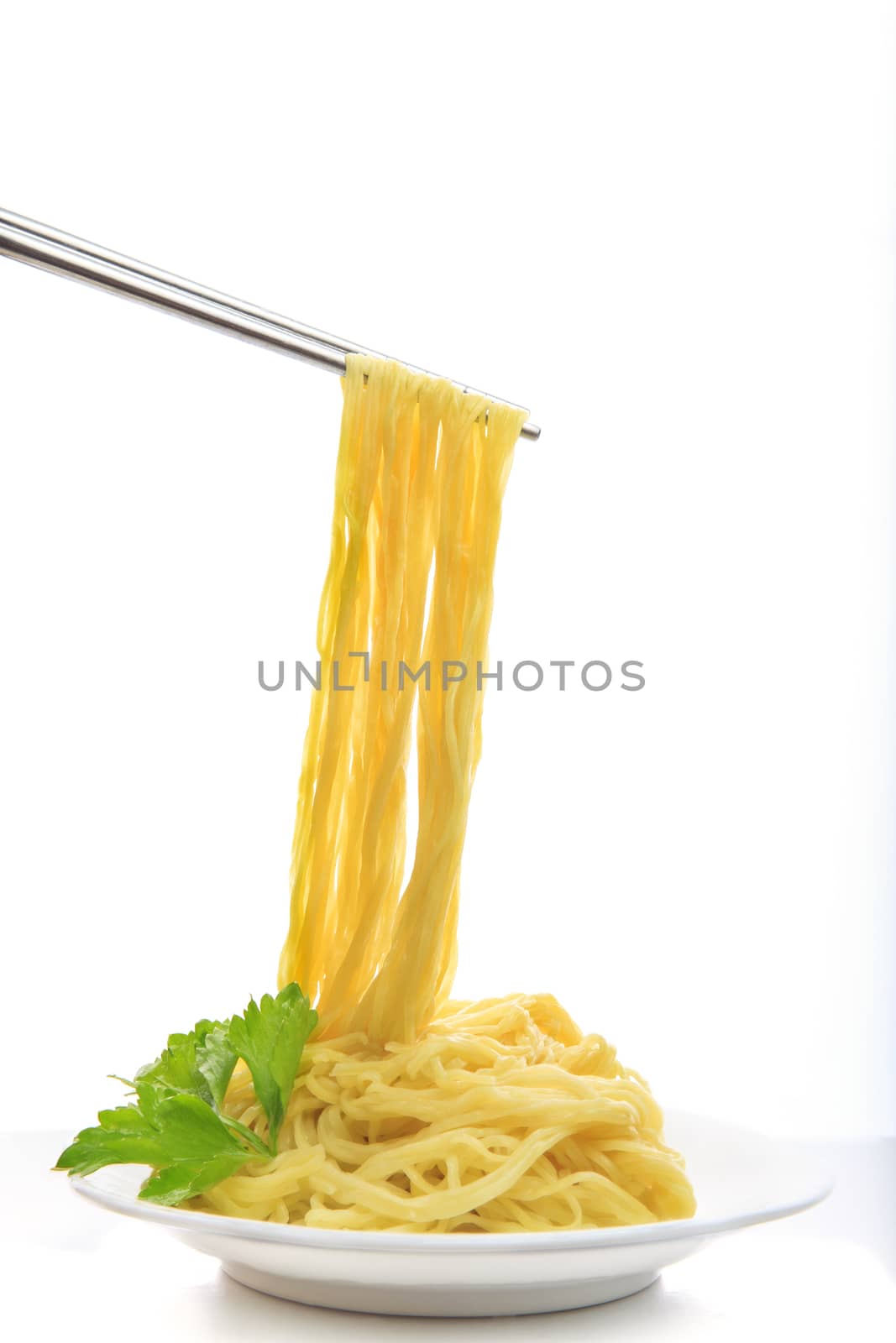 steel chopstick holding chinese yellow eggs noodle on white disk with green leaves of  celery ready to eating meal on white background 